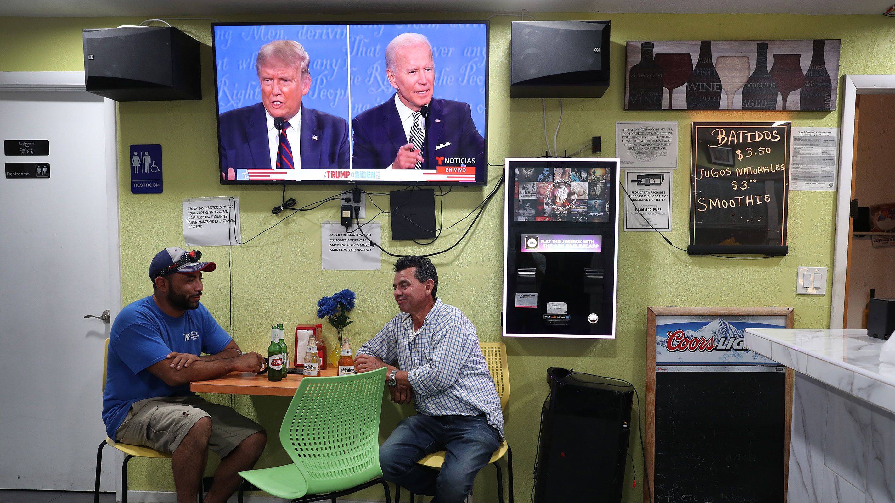 Raul Ortiz and Jose Martin sit in a restaurant under a TV broadcasting the first debate between then-President Donald Trump and then-Democratic presidential nominee Joe Biden in Miami on September 29, 2020.