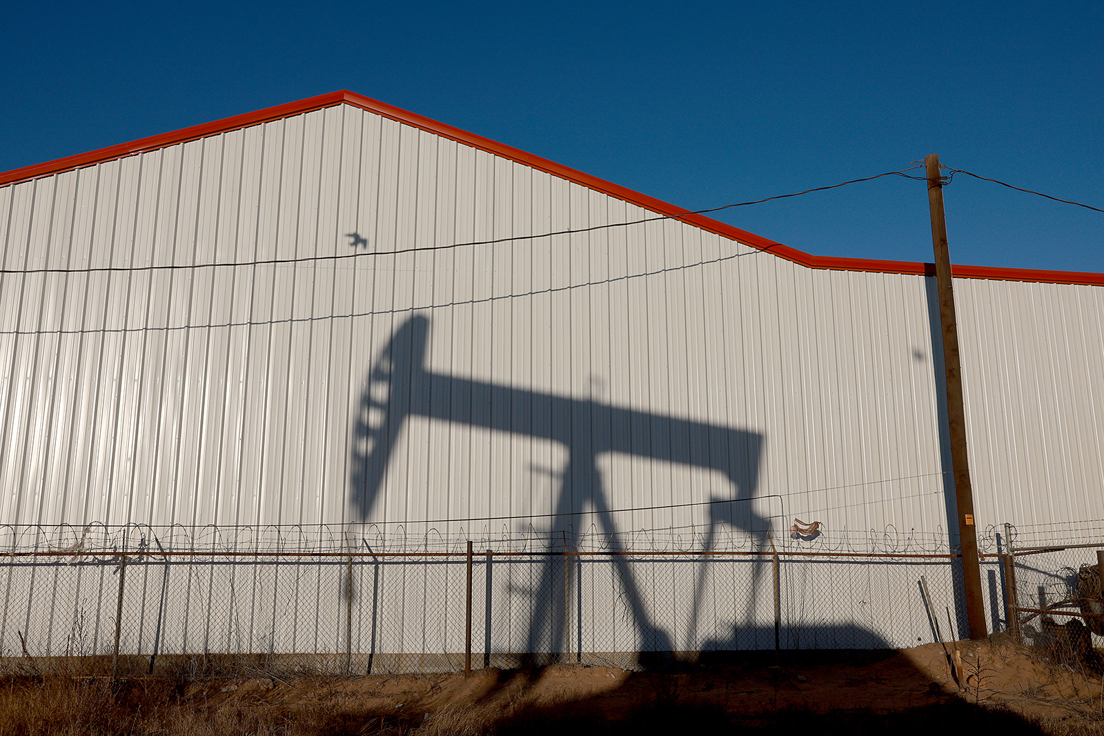 An oil pumpjack casts a shadow on a wall as it pulls oil from the Permian Basin oil field on March 14, 2022 in Odessa, Texas. 