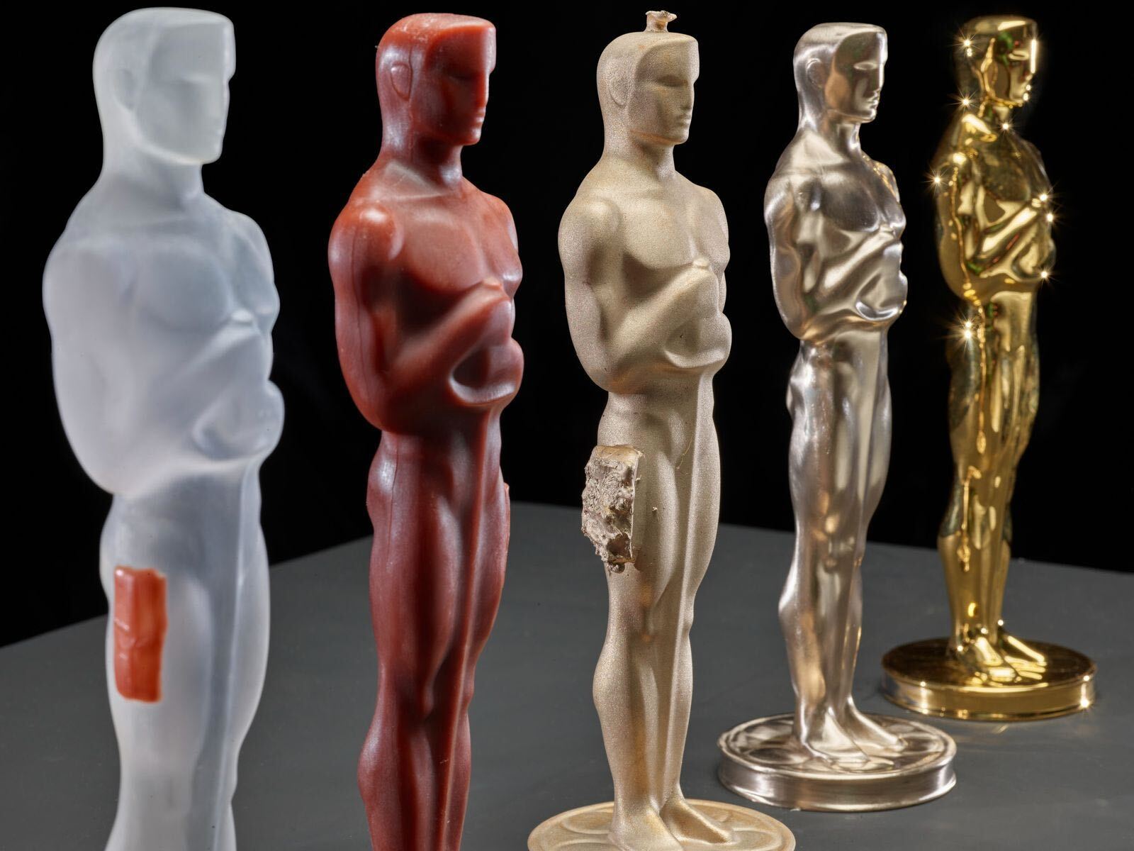 A look at Oscar statuettes at various steps of the manufacturing process — from the 3D-printed model on the left to the final gold-plated version on the right.