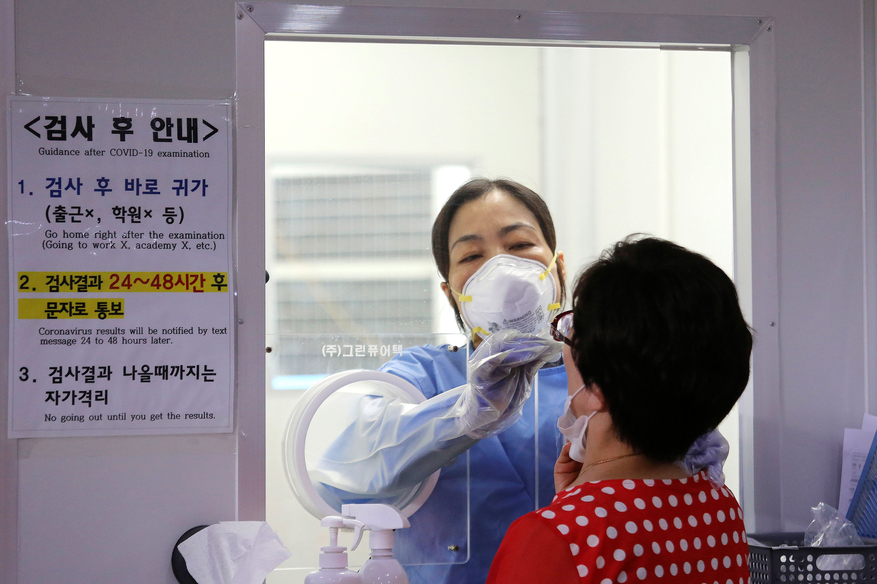 A medical worker in a booth takes a coronavirus test swab sample from a woman on August 26 in Seoul, South Korea. 