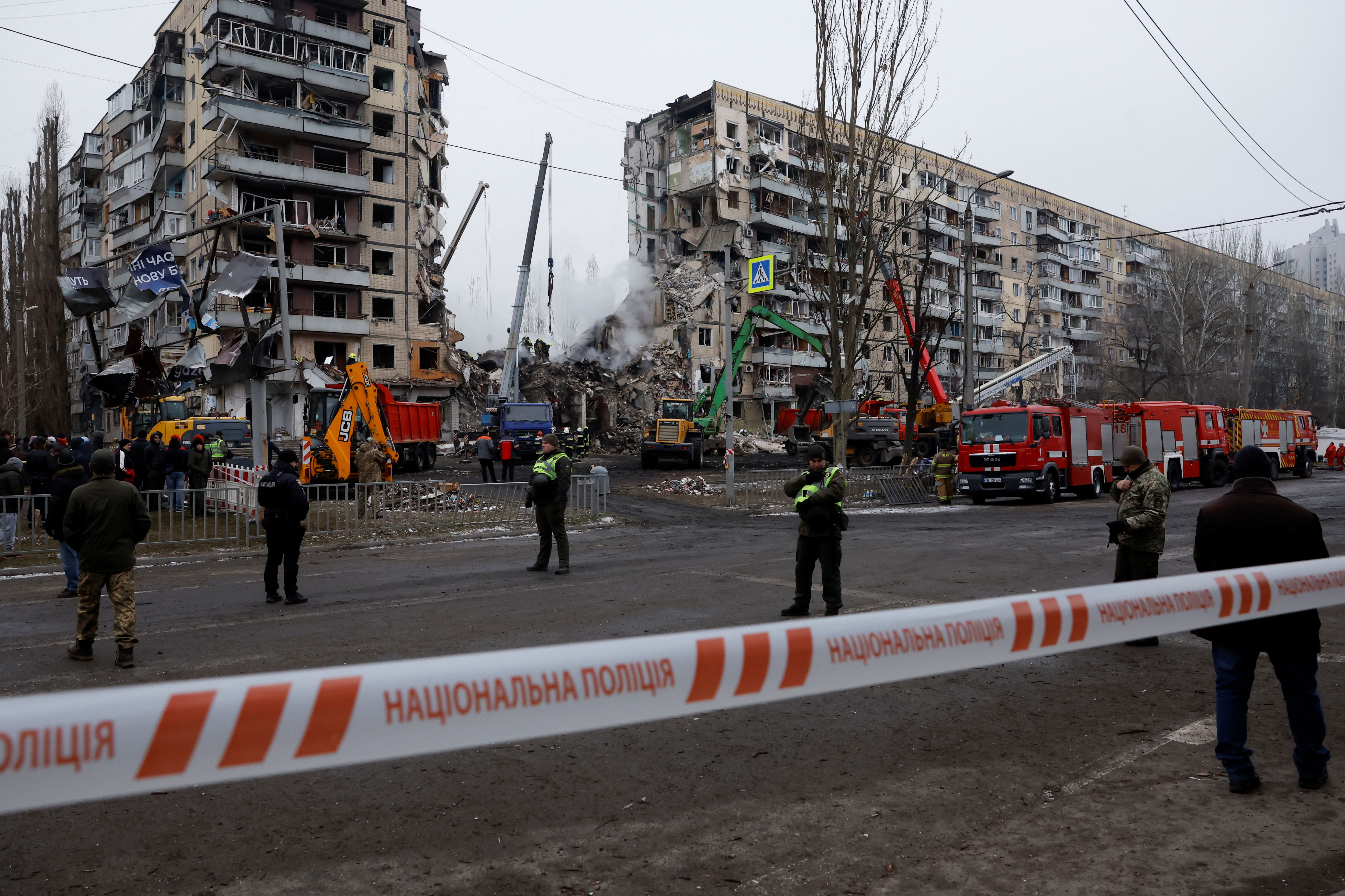People watch as emergency personnel work at the site where an apartment block was heavily damaged by a Russian missile strike in Dnipro on Sunday.