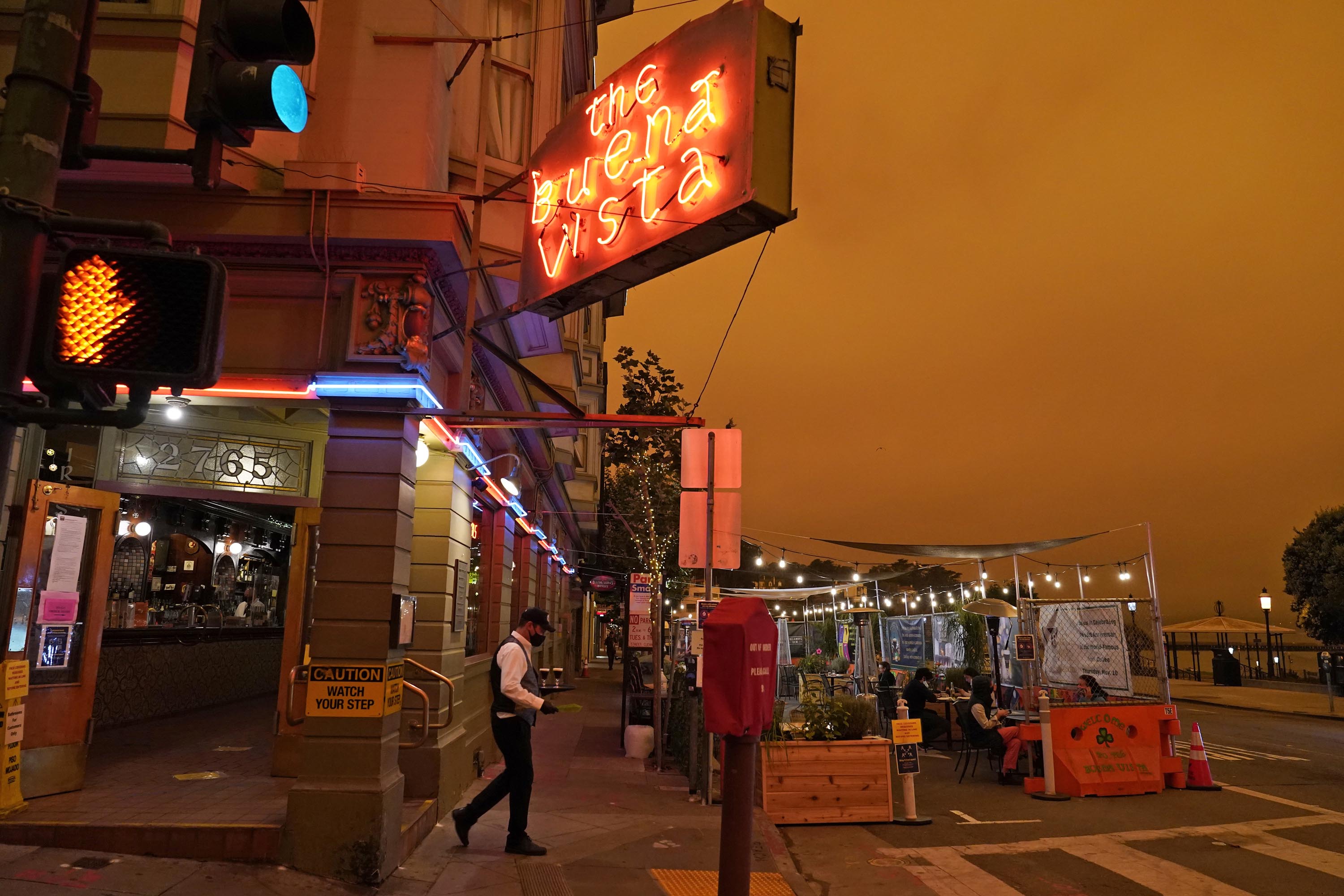 A waiter carries a tray to people having lunch at the Buena Vista Cafe in San Francisco, under darkened skies from wildfire smoke, on Wednesday.