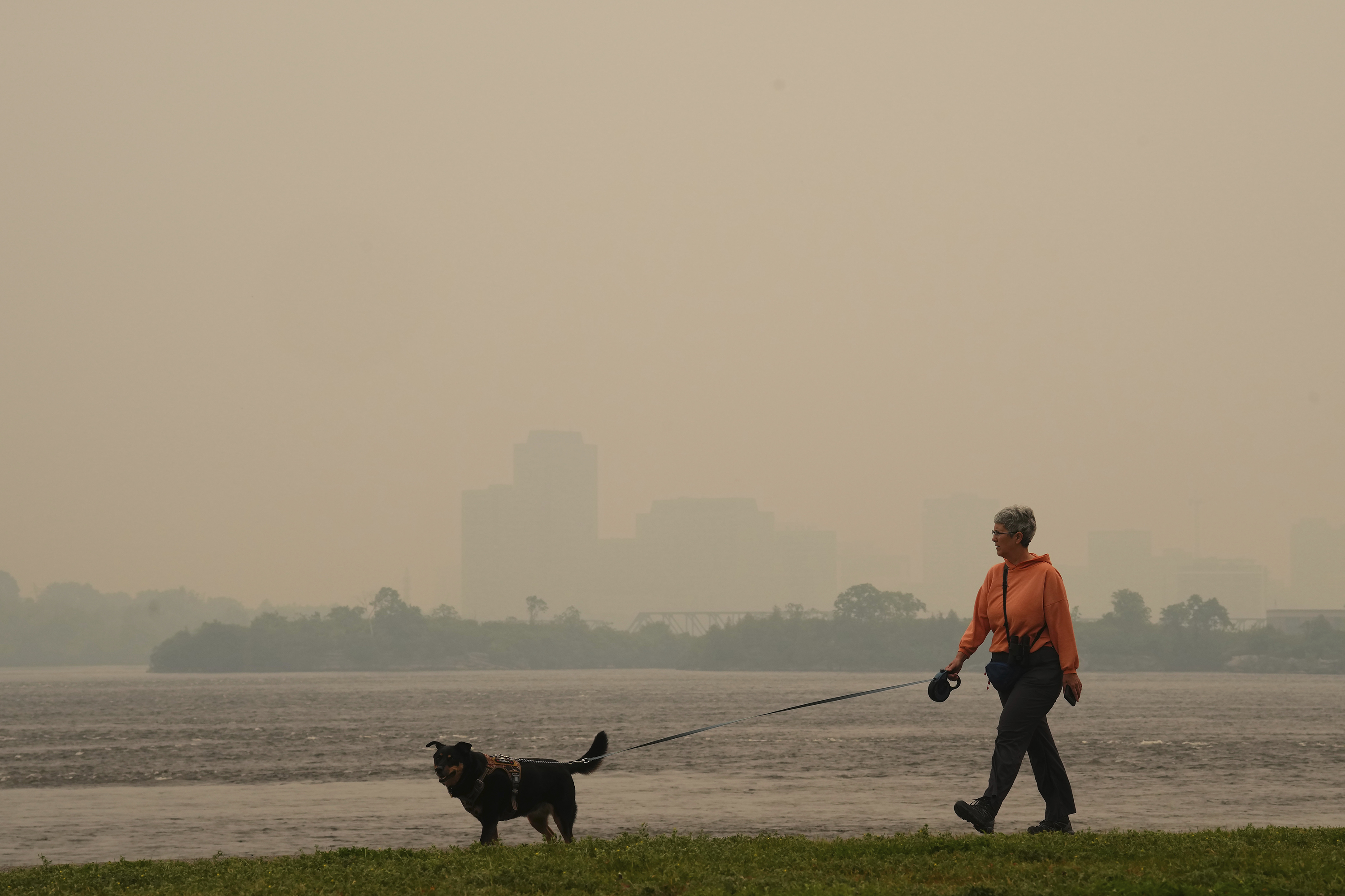A woman walks her dog along the Ottawa River in Ottawa as smoke from wildfires obscures Gatineau, Quebec, in the distance on June 6.