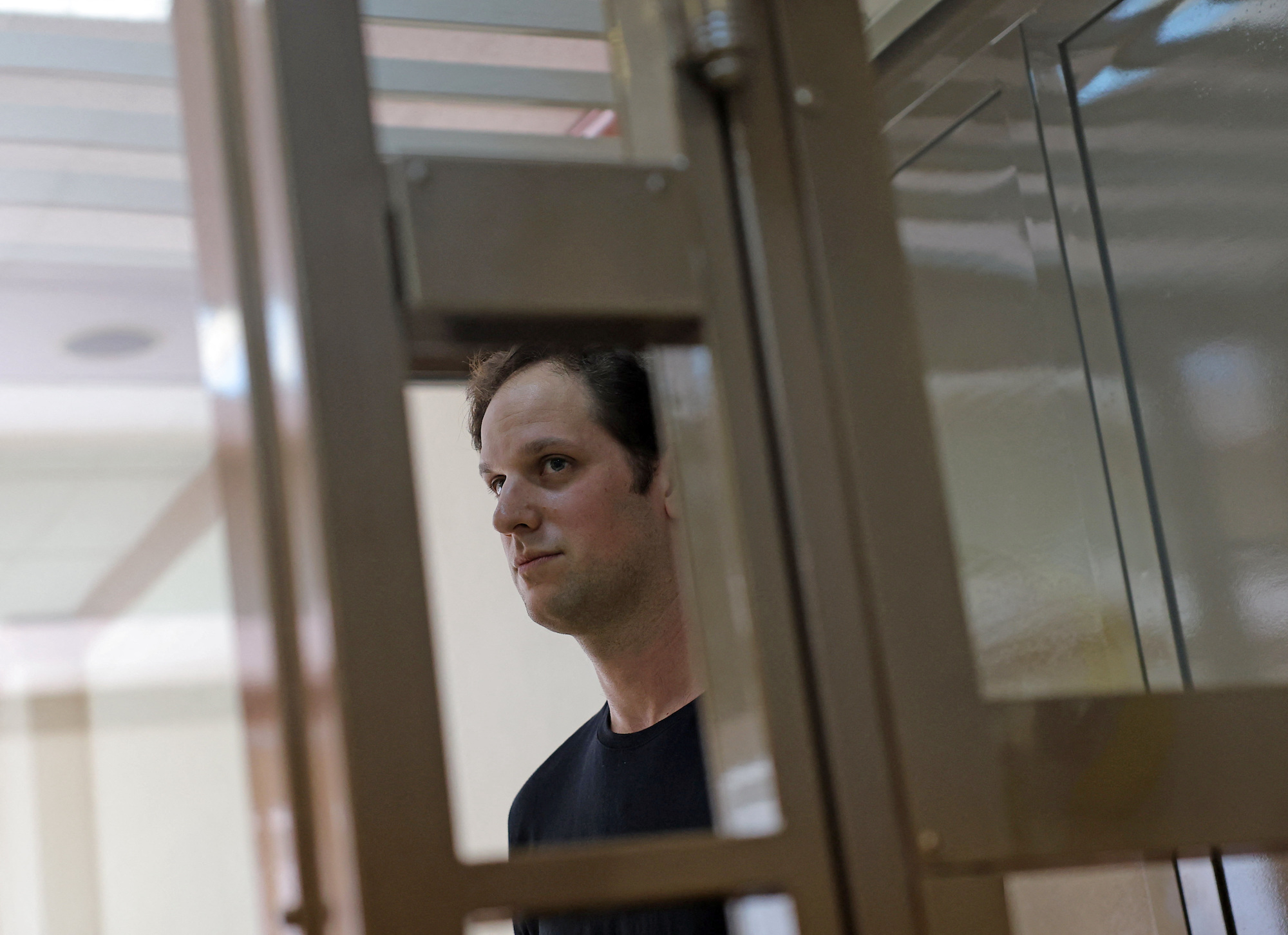 WSJ reporter Evan Gershkovich stands behind a glass wall of an enclosure at a court hearing in Moscow on Thursday.
