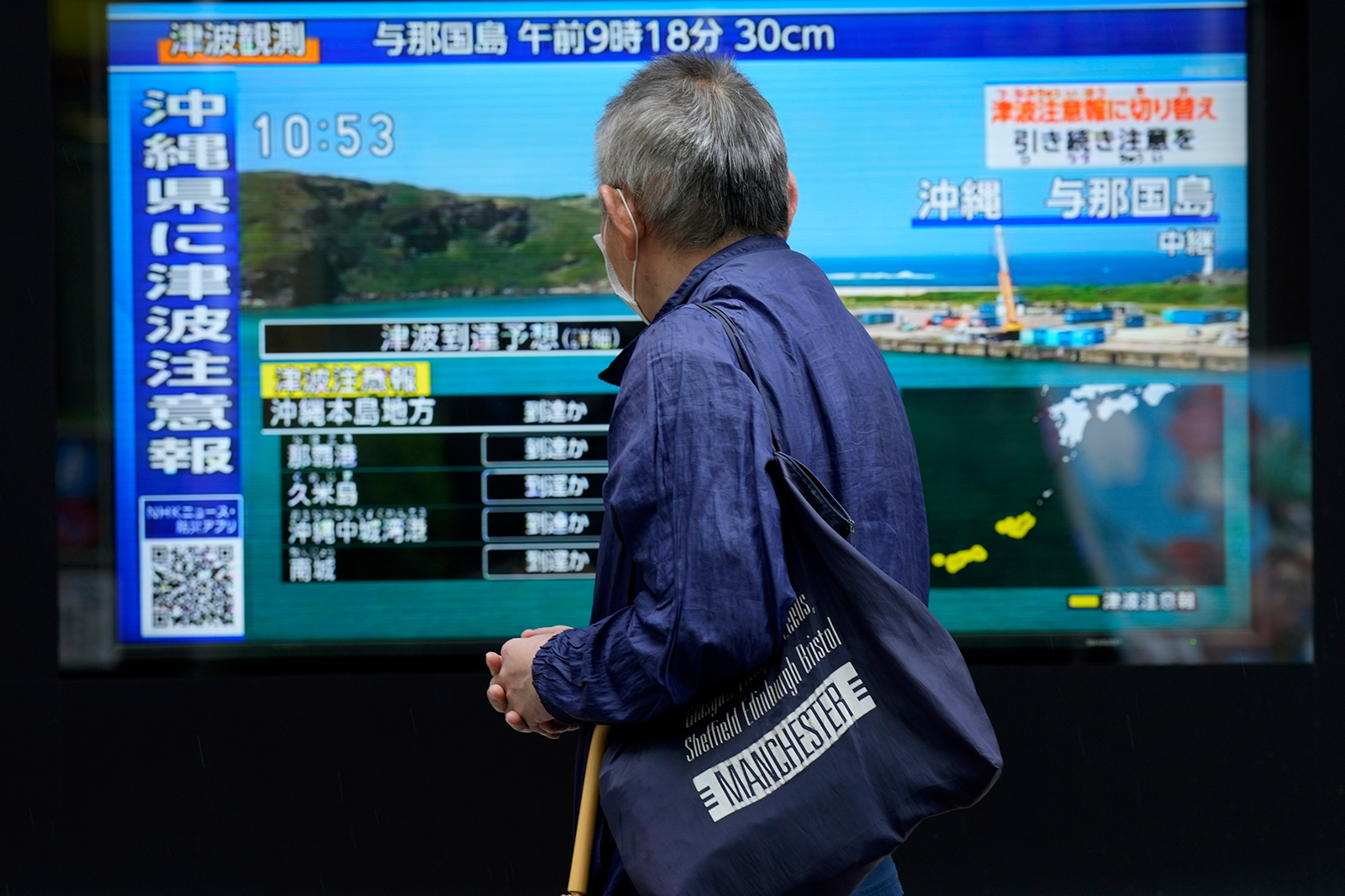 A man stands along a sidewalk to watch a TV showing breaking news on the tsunami advisory for the Okinawa region on Wednesday, April 3, in Tokyo. 