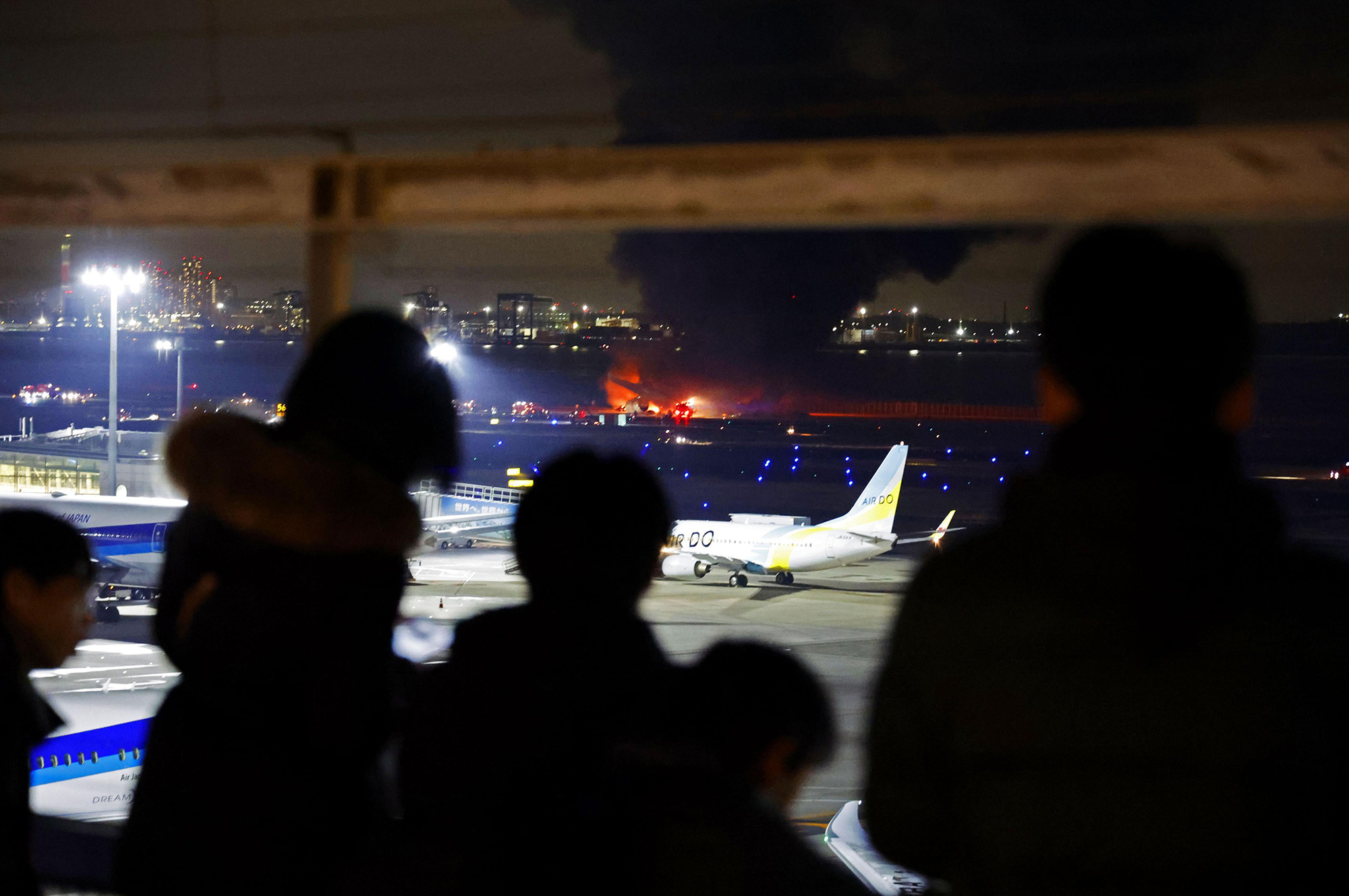 Onlookers watch as a Japan Airlines airplane burns on a runway at Haneda International Airport in Tokyo, on January 2. 
