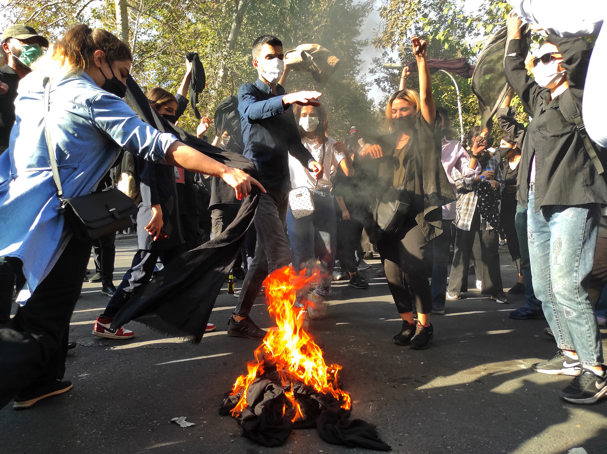 Iranian protesters set their scarves on fire while marching down a street on October 1 in Tehran, Iran. 