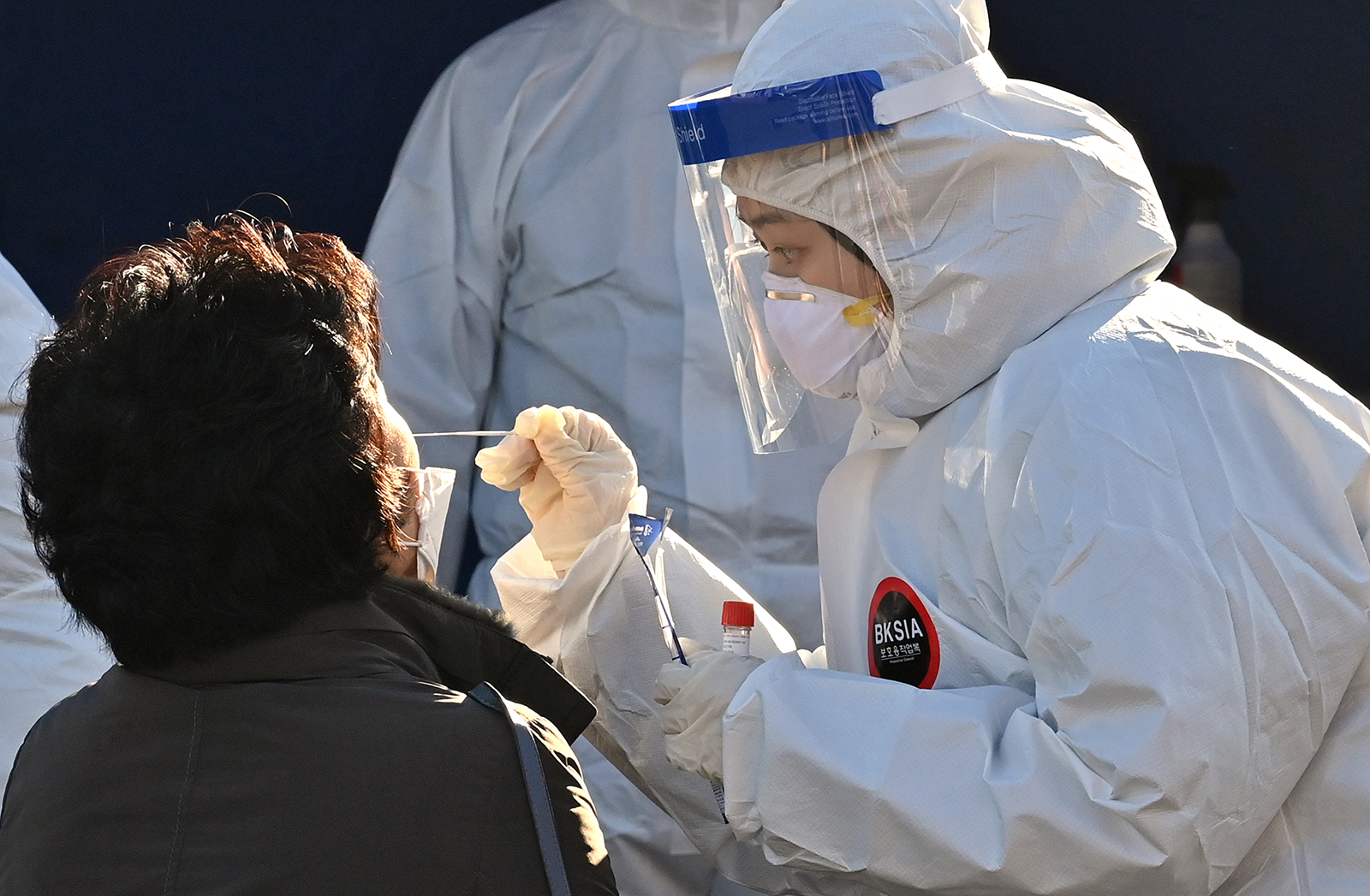 A medical staff member wearing protective gear takes a swab from a woman to test for Covid-19 at a temporary testing station in Seoul, South Korea, on December 14.