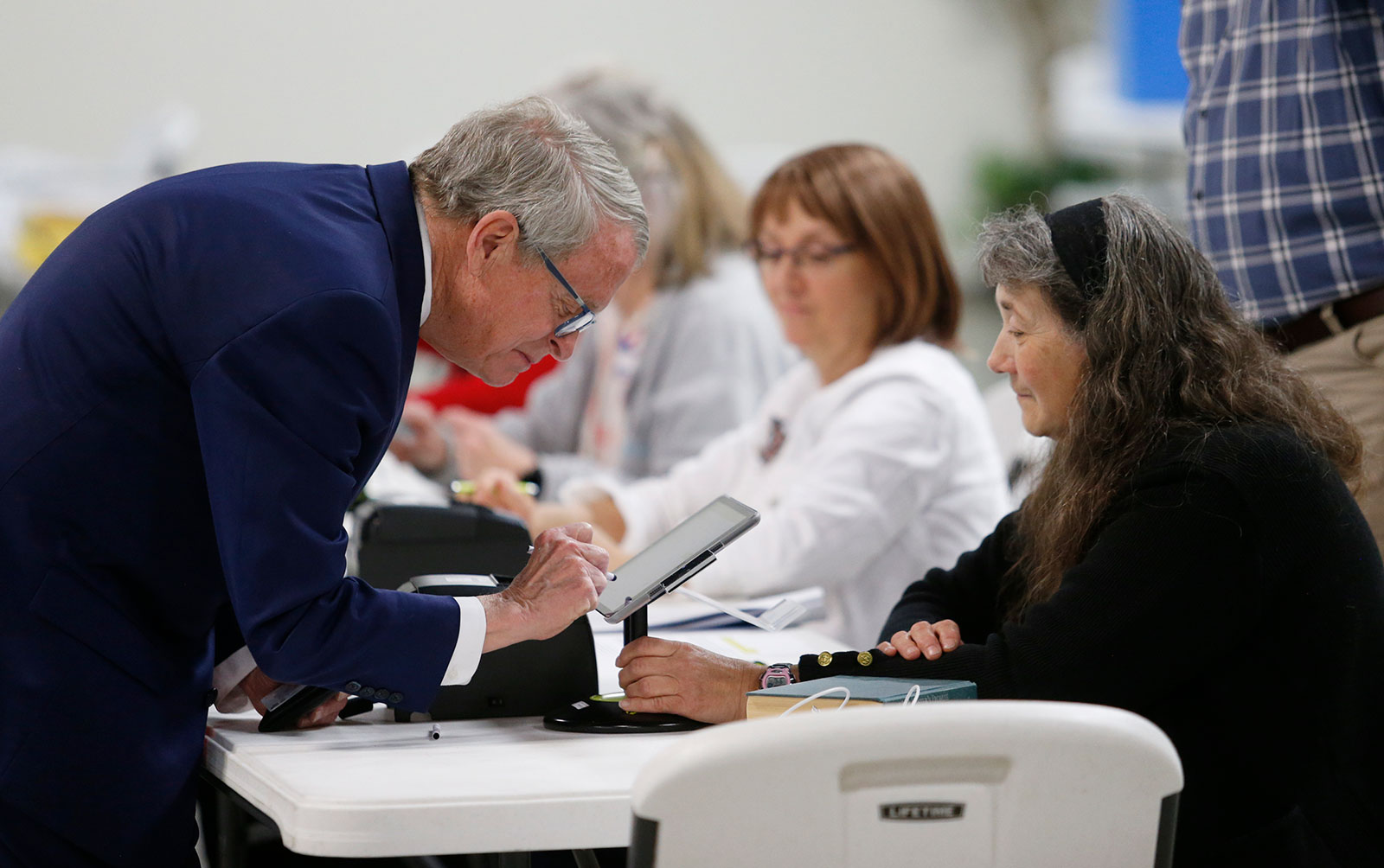 Ohio Gov. Mike DeWine, left, signs for his ballot in front of precinct worker Tonya Veldt as he prepares to vote in Cedarville, Ohio, on Tuesday, May 3.