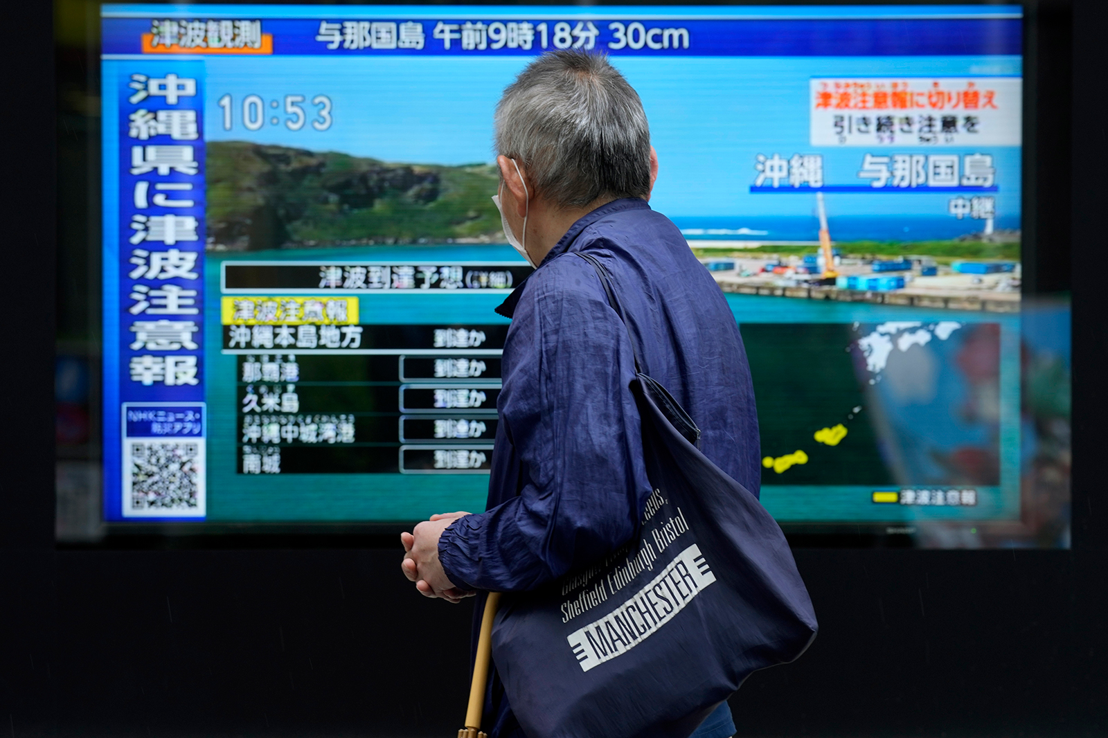 A man stands along a sidewalk in Tokyo to watch a TV showing breaking news on a tsunami warning for Okinawa on April 3, 2024. 