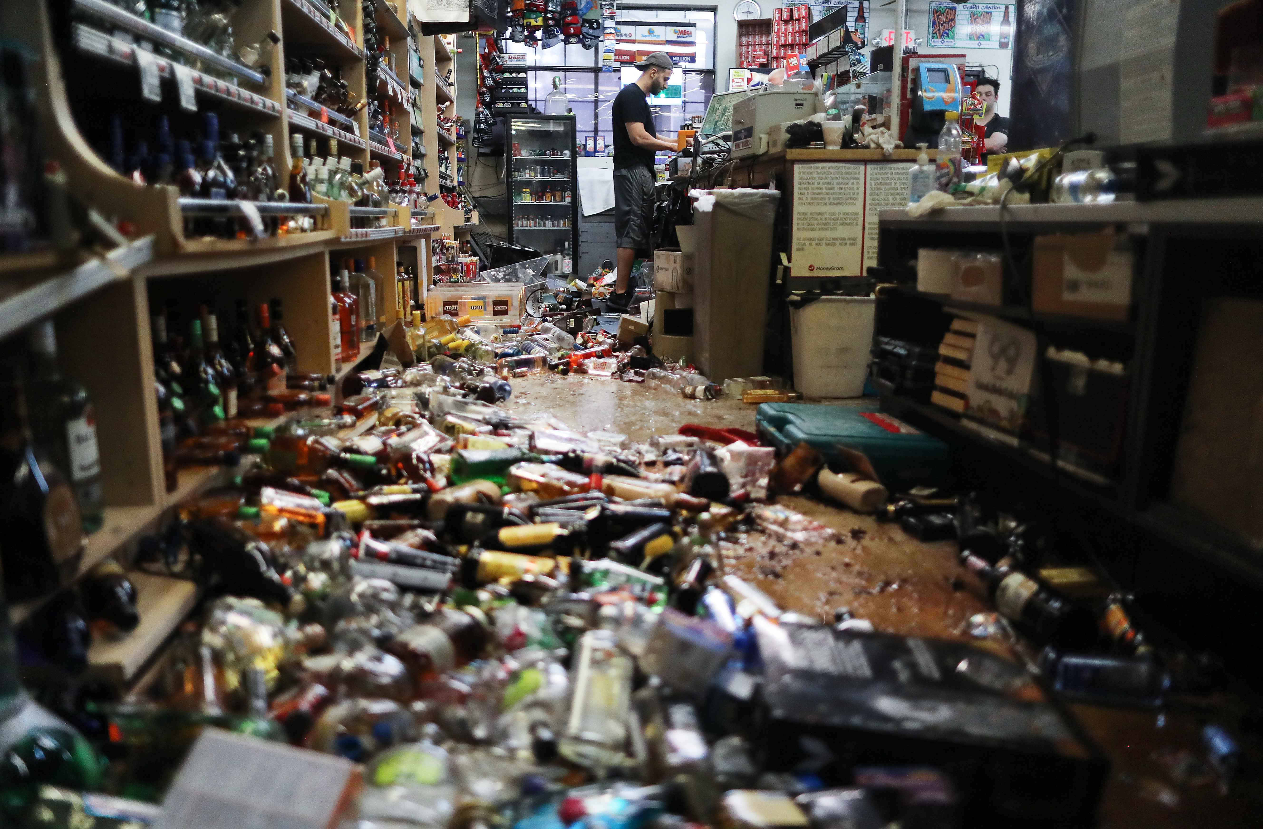 An employee works at the cash register at Ridgecrest Market, near broken bottles scattered on the floor, following a 7.1 magnitude earthquake. 