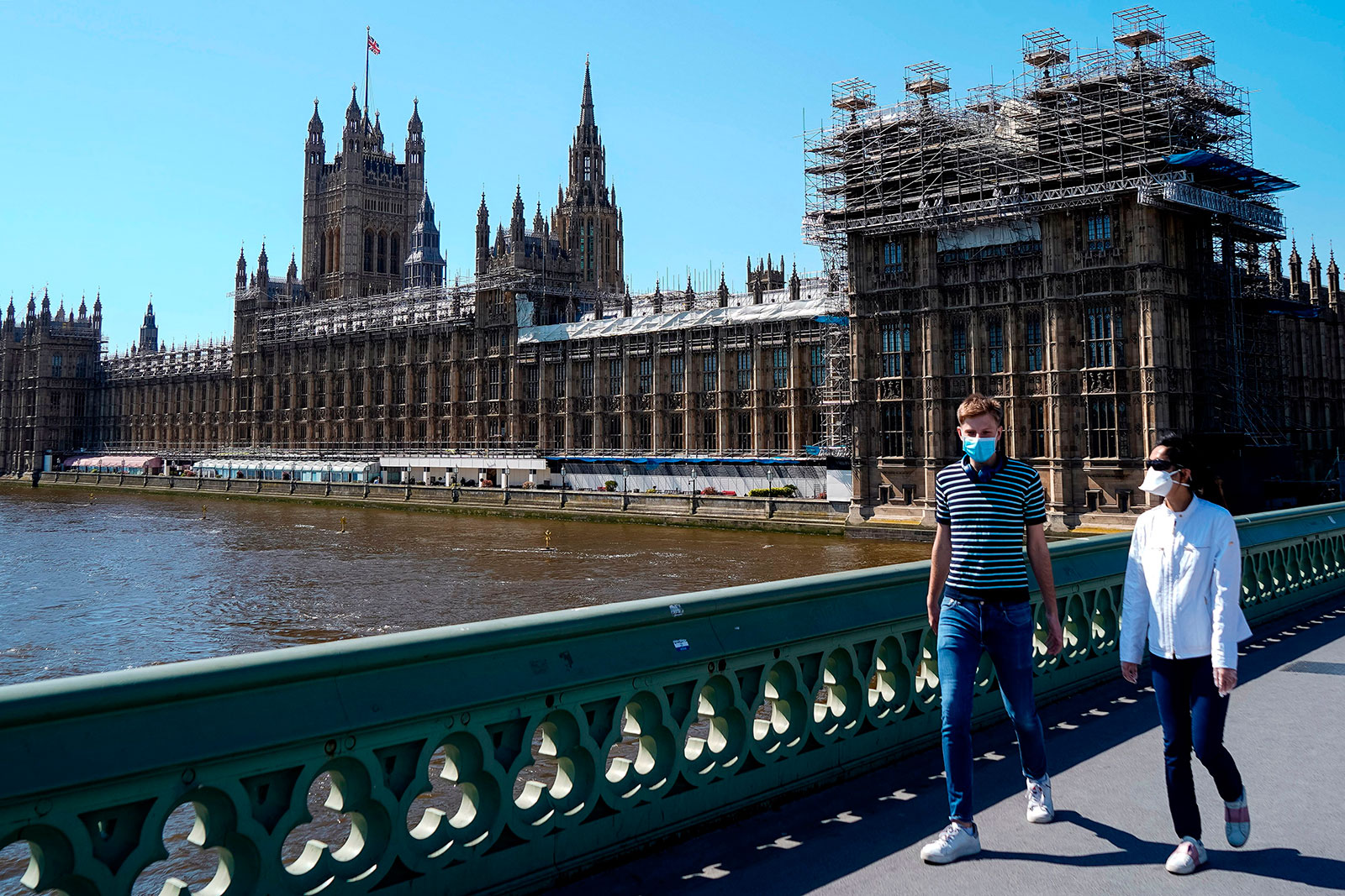 A couple wearing protective face masks walk over Westminster Bridge in front of the Palace of Westminster in central London on April 20.