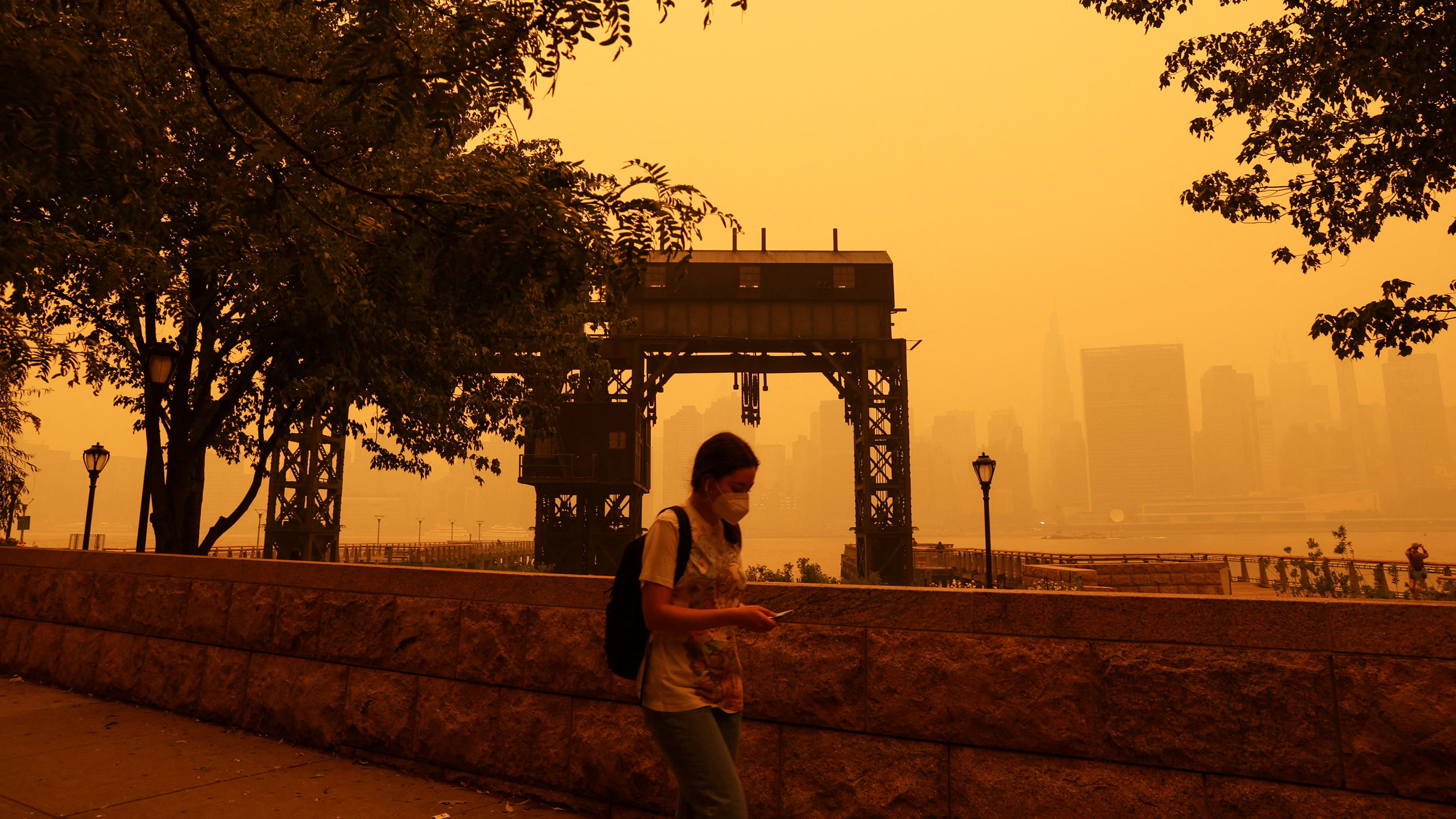 A woman wearing a protective mask walks at Gantry Plaza State Park as haze and smoke from the Canadian wildfires shroud the Manhattan skyline in the Queens Borough of New York City on June 7, 2023.