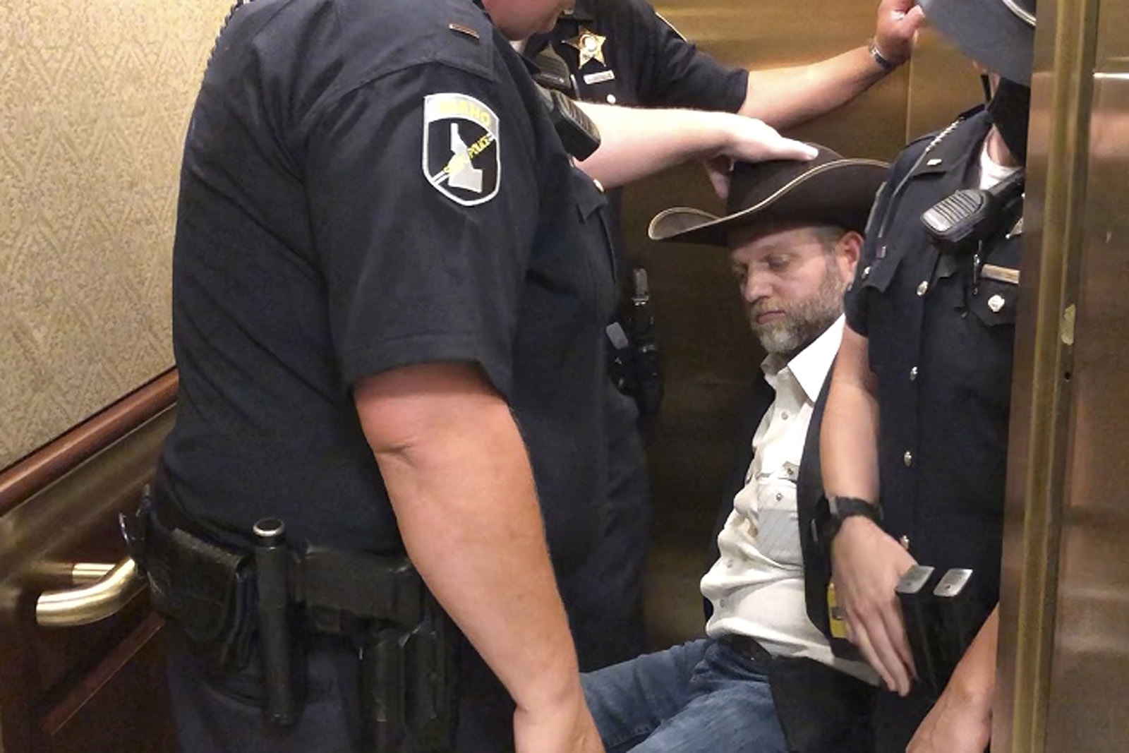This image taken from video shows anti-government activist Ammon Bundy, rear, being wheeled into an elevator in a chair following his arrest at the Idaho Statehouse in Boise, Idaho, Tuesday, August 25.