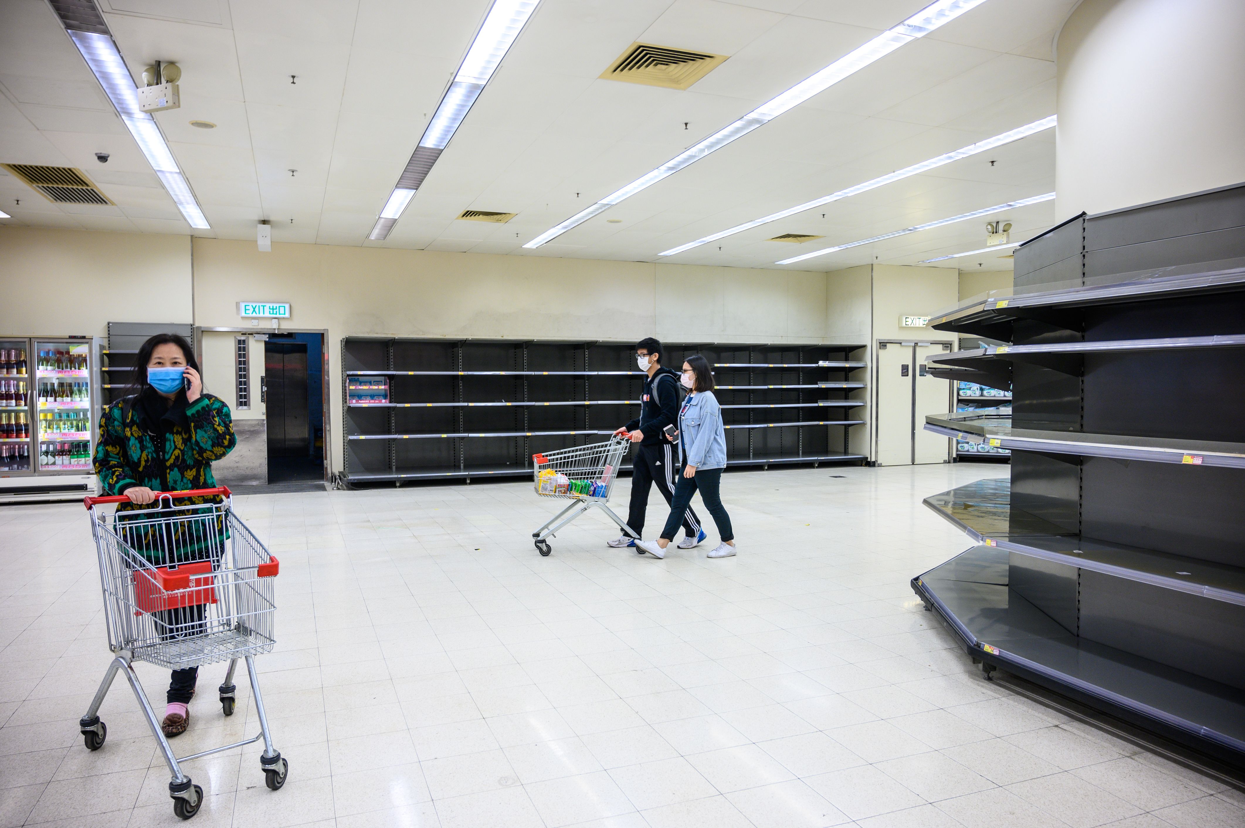 Shoppers wearing protective facemasks walk past bare supermarket shelves, usually stocked with toilet paper and kitchen rolls, in Hong Kong on Thursday.