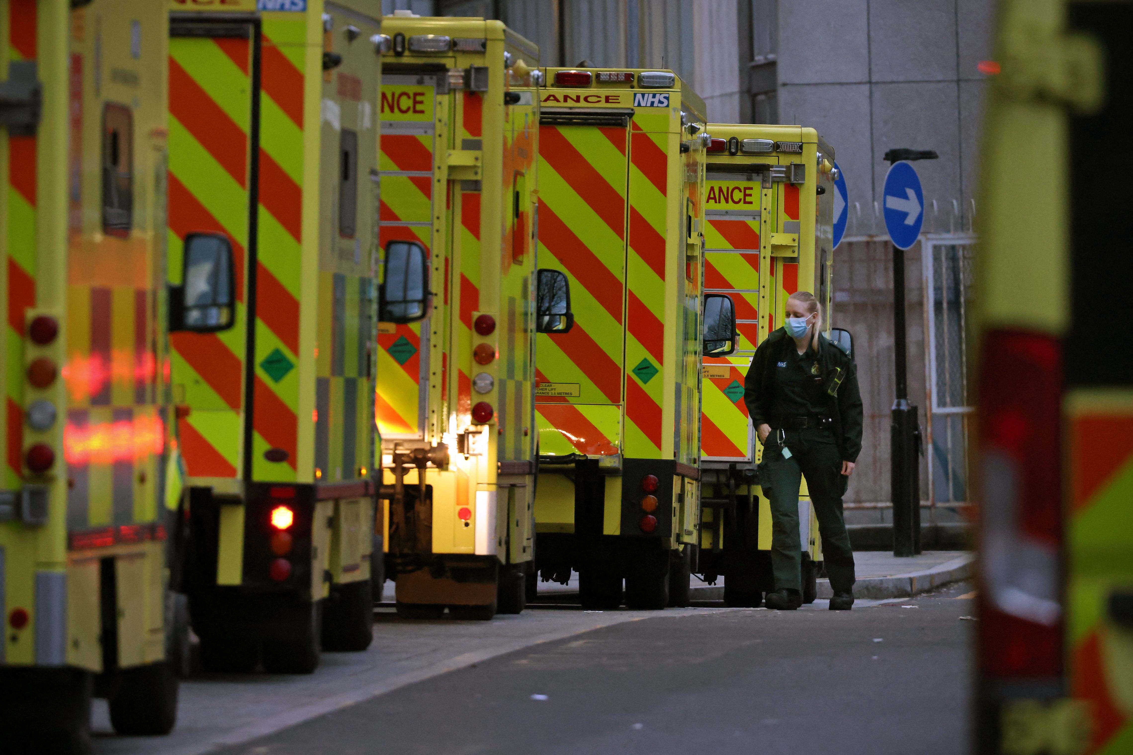 An Ambulance crew member is seen alongside ambulances parked outside the Royal London hospital in London on December 28, 2021. - England has been pressing ahead with its Covid-19 immunisation campaign in the race to inoculate as many people possible while the number of cases of the Omicron coronavirus variant soars.