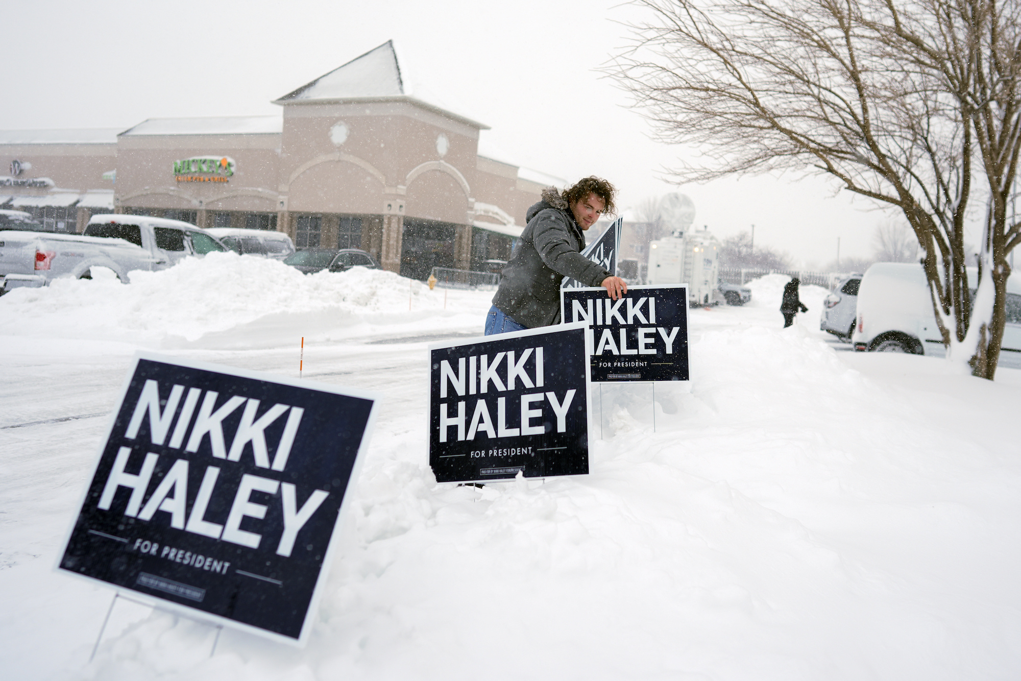 A campaign worker places signs in a snow bank before a campaign event for Nikki Haley in Waukee, Iowa, on Tuesday.