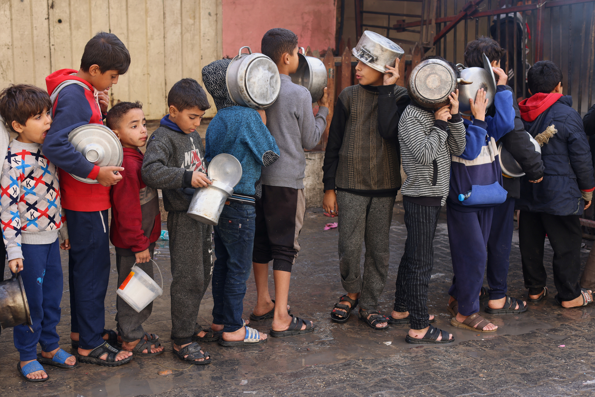 Palestinian children hold pots as they queue to receive food cooked by a charity kitchen, amid shortages in food supplies, in Rafah, southern Gaza, on December 14.