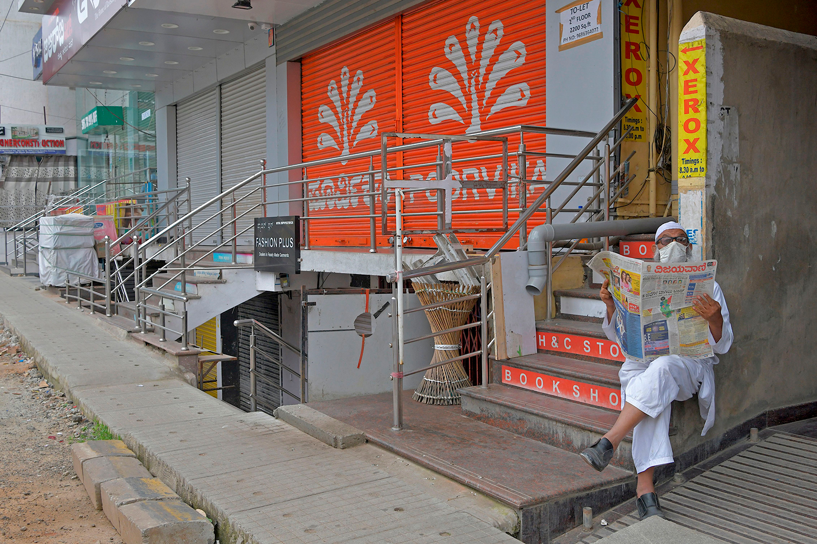 A man reads a newspaper while sitting in front of closed shops in a commercial area in Bangalore, India on July 15.