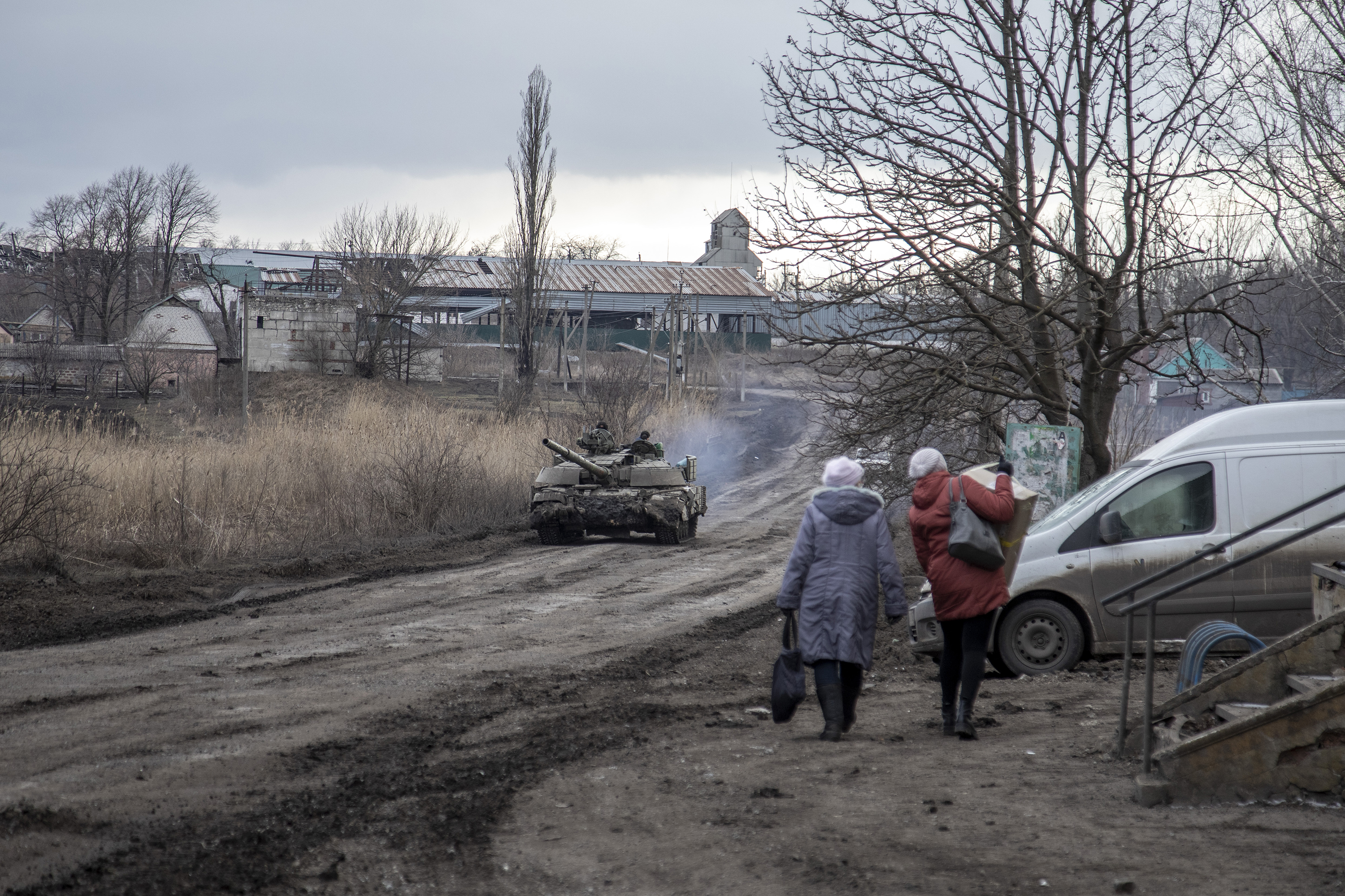 Civilians walk on a road as a tank drives by in a village nearby Avdiivka frontline on February 20.