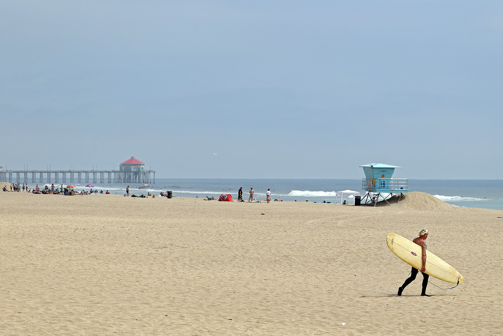 A surfer walks on the beach in front of the pier on April 30, in Huntington Beach, California.