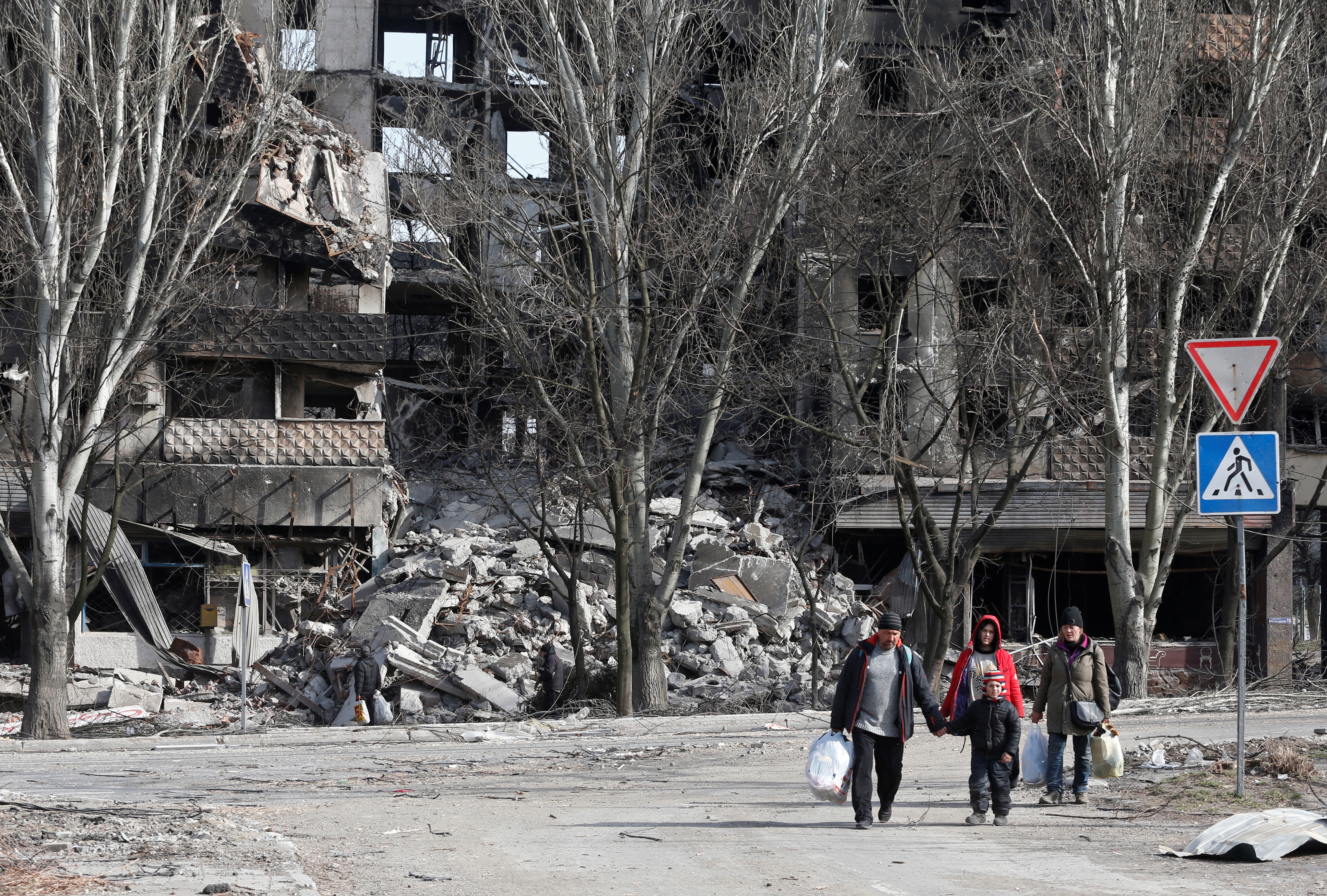 Local residents walk past a destroyed apartment building in the besieged southern port city of Mariupol, Ukraine, on March 31.