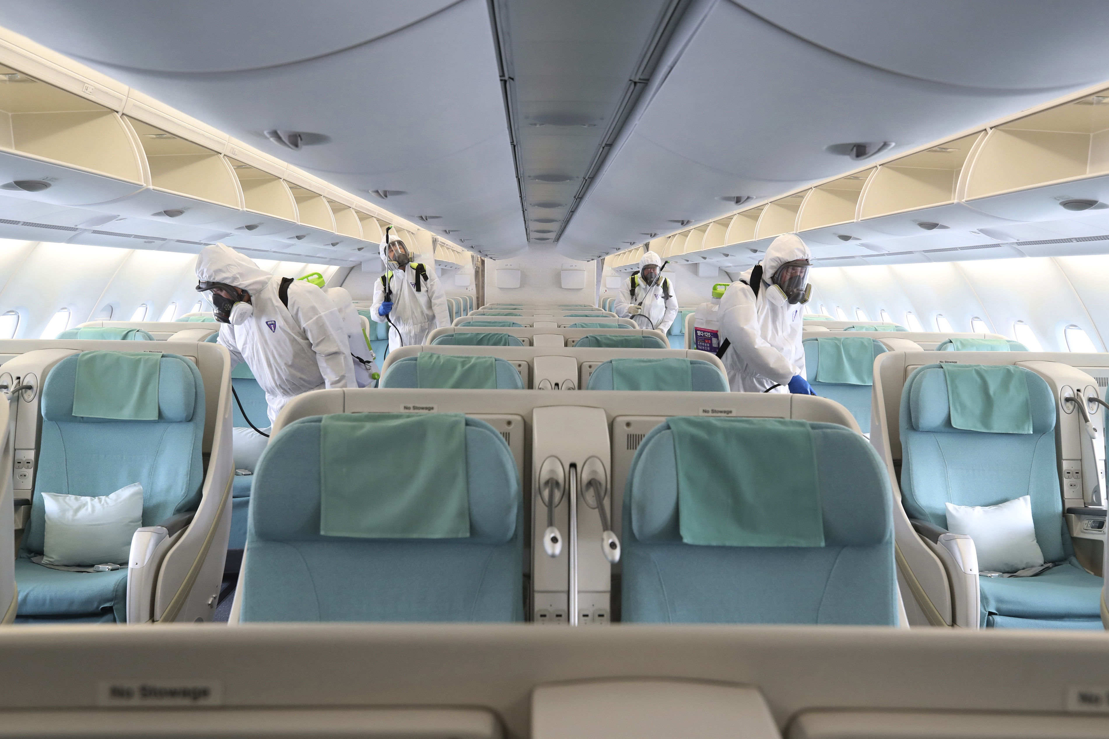 Workers wearing protective gears spray disinfectant inside an airplane bound for New York at Incheon International Airport in Incheon, South Korea, on Wednesday, March 4.