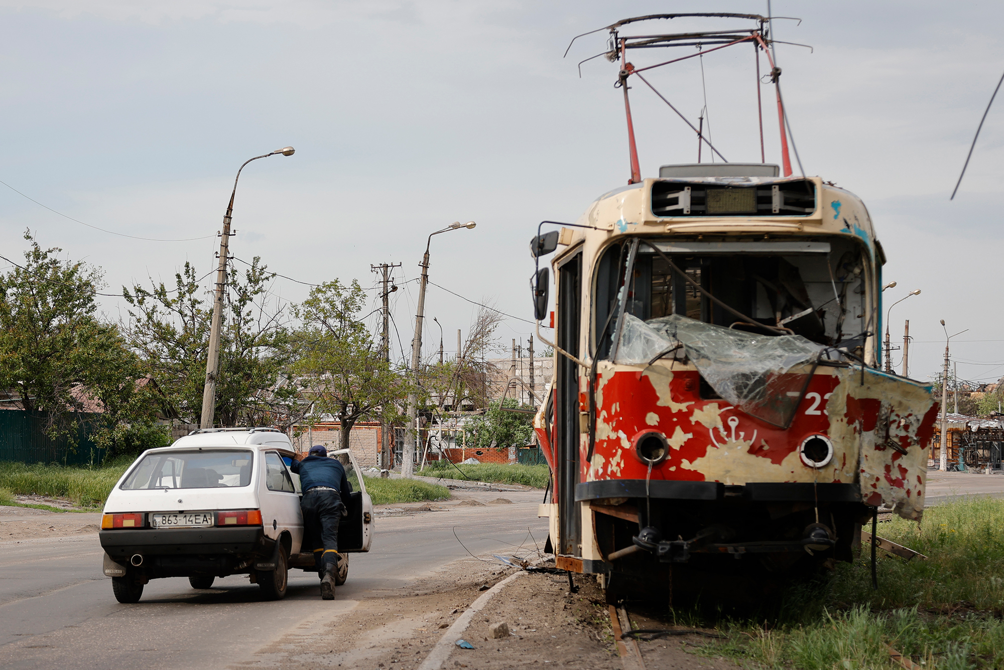 Un hombre empuja un automóvil estacionado frente a un tranvía dañado en Mariupol el 21 de mayo. 