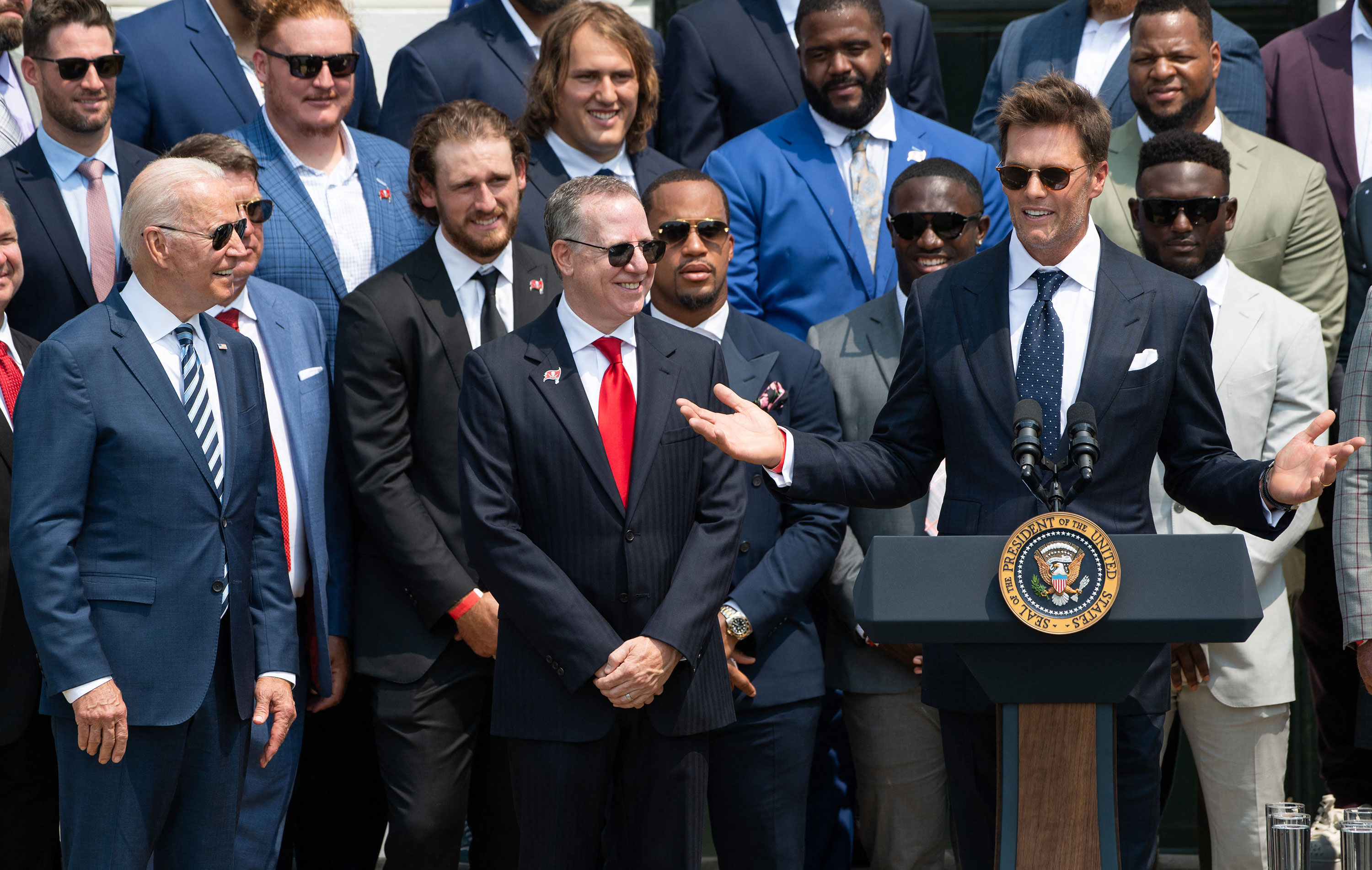 President Joe Biden, left, and Tampa Bay Buccaneers owner Bryan Glazer, center, listen as Tom Brady speaks during a ceremony at the White House honoring the Buccaneers' Super Bowl win in July.