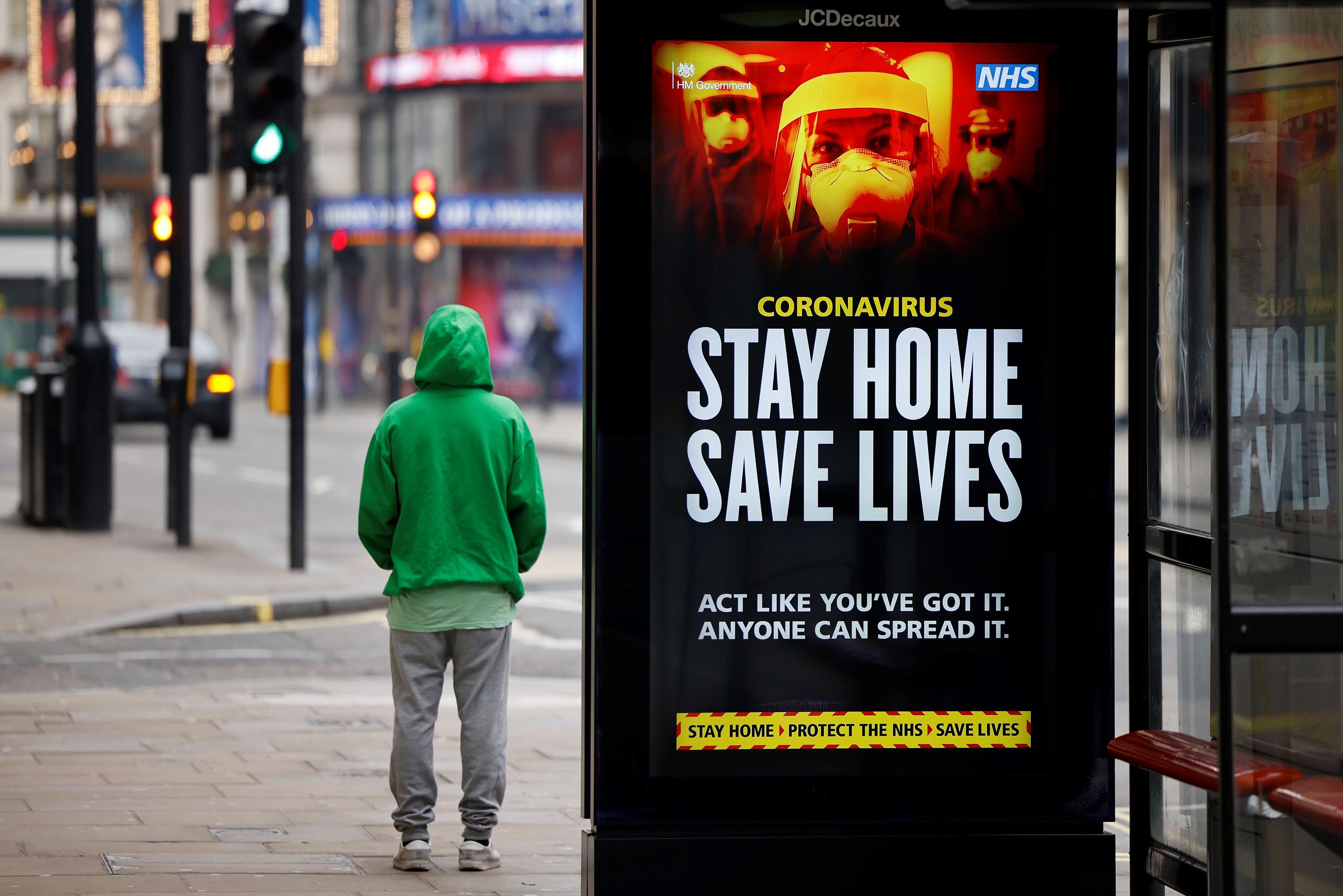 A man stands near signage promoting the UK's National Health Service message, 