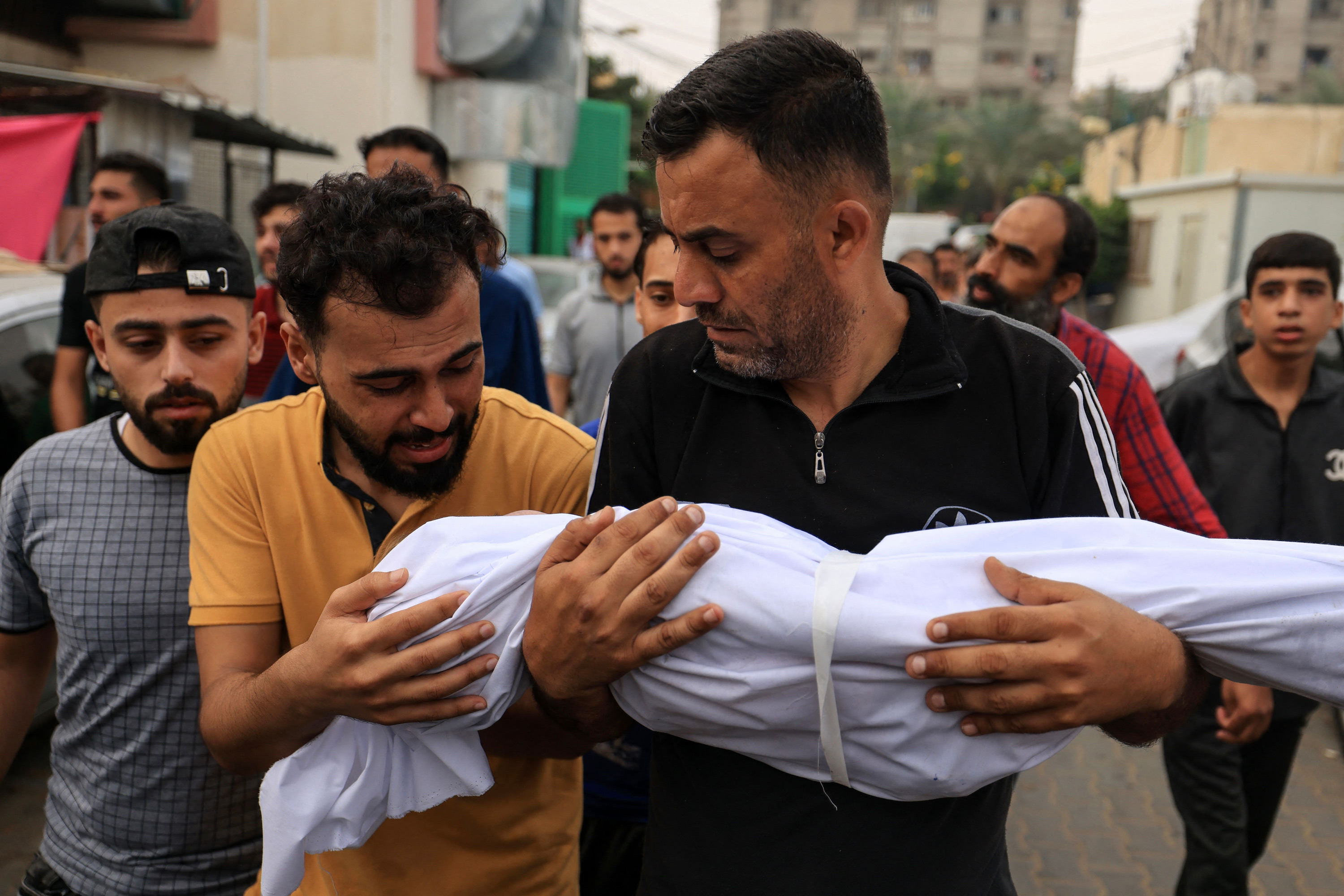 The father of a young boy from the al-Aqad family, reacts as he touches the body of his child, killed in an Israeli strike on Khan Younis, southern Gaza, before his burial on October 29.