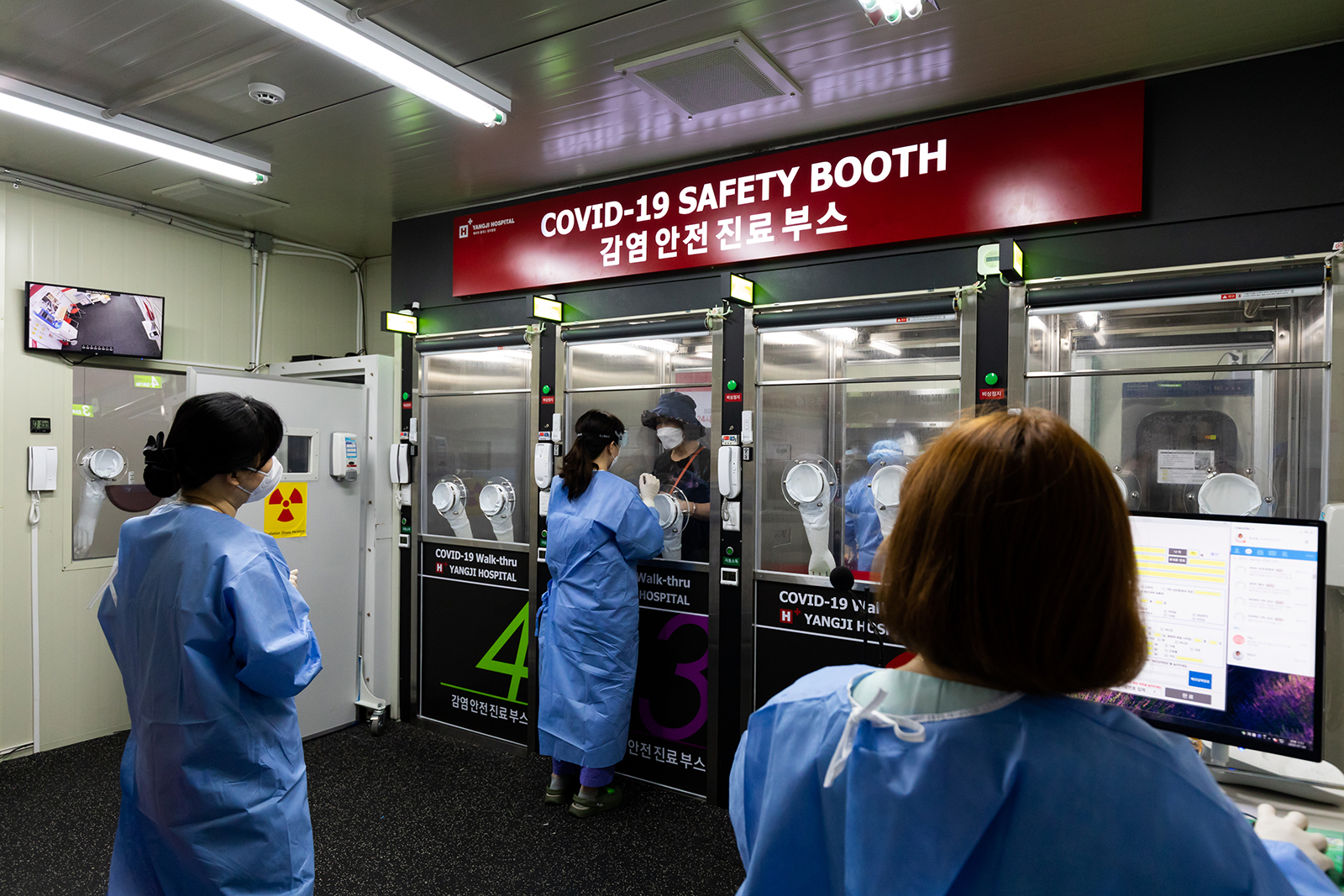 A medical worker wearing personal protective equipment (PPE), center, speaks with a visitor from inside the Covid-19 safety booth in the walk-thru testing center at H Plus Yangji Hospital in Seoul, South Korea, on July 24.