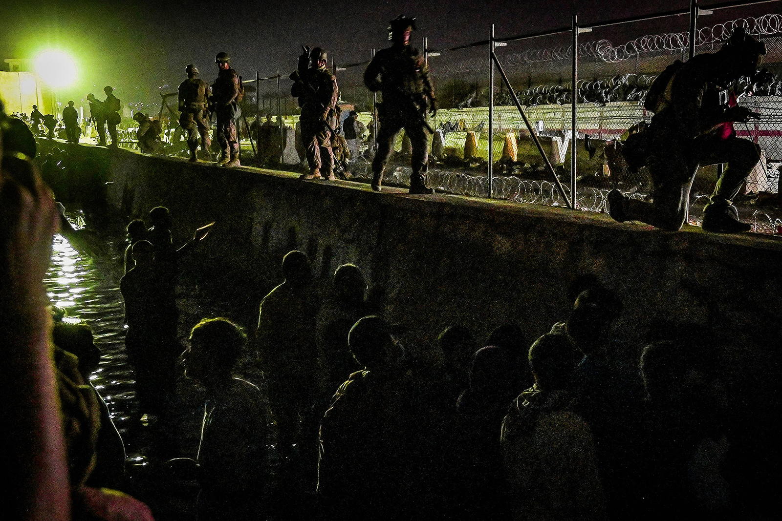 Soldiers stand guard near a canal as Afghans wait outside the foreign military-controlled part of the airport in Kabul, hoping to flee the country following the Taliban's military takeover of Afghanistan, on August 22.