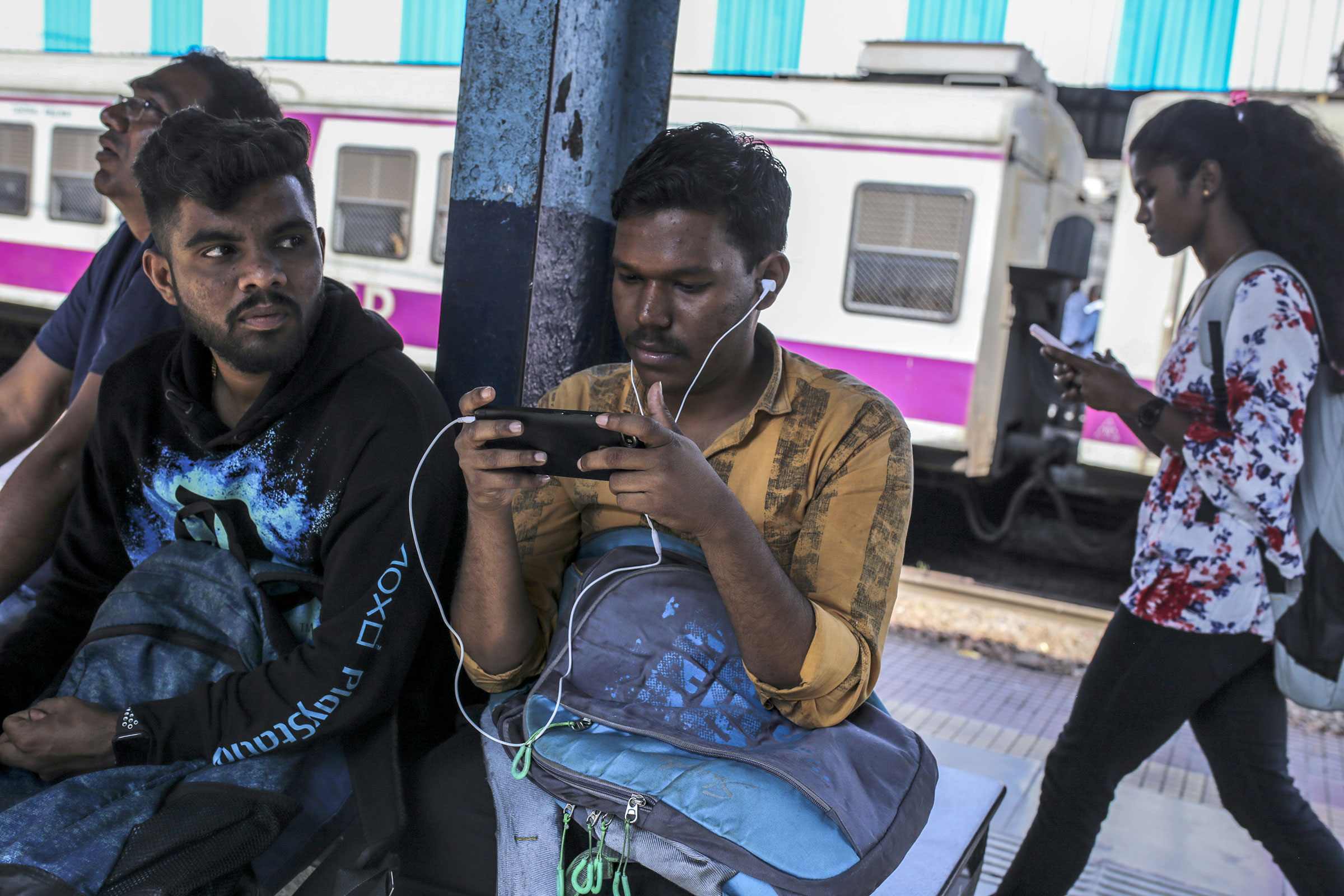 Passengers use smartphones while sitting on a platform of a railway station in Mumbai, India, in February 2020.