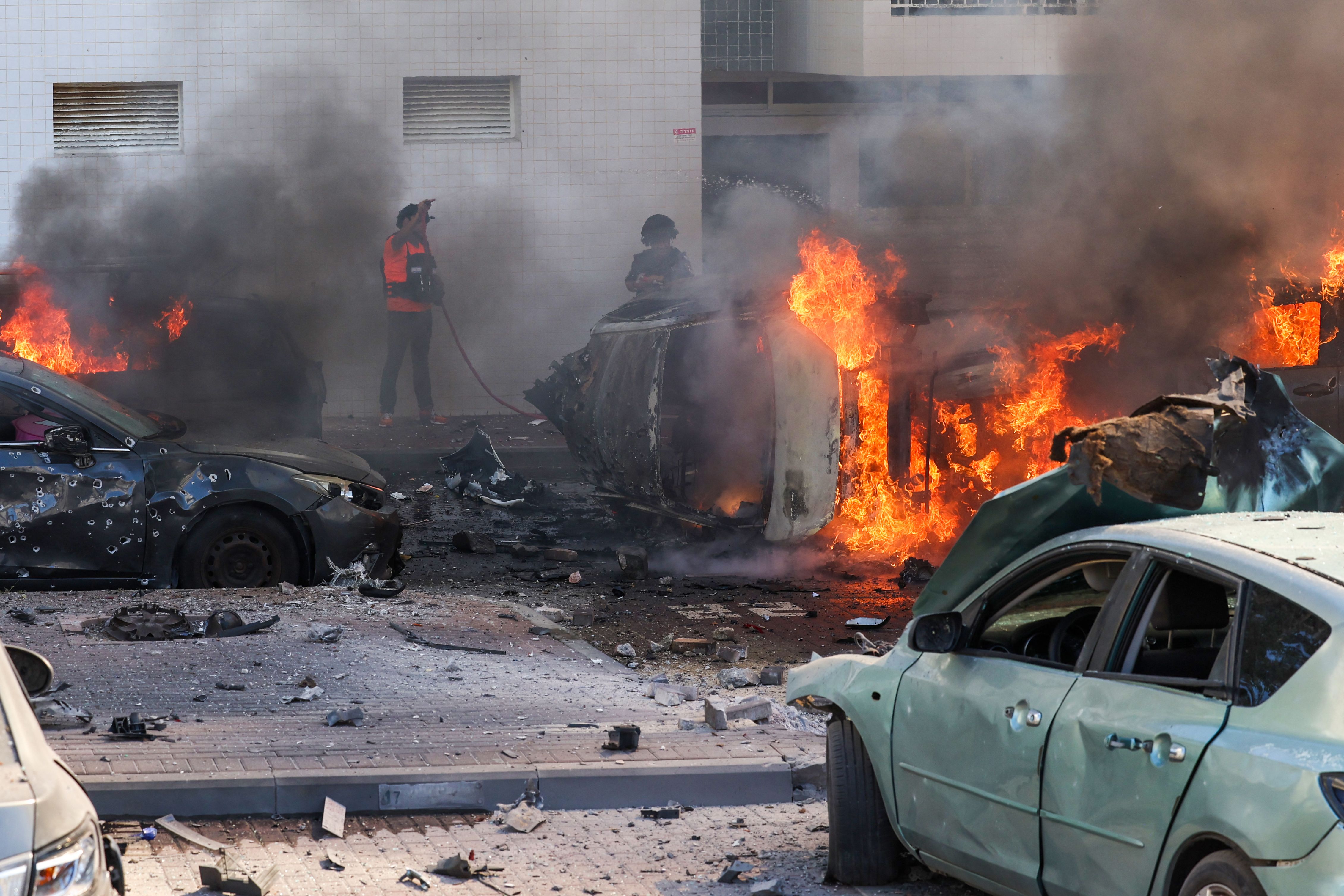 People try to extinguish fire on cars following a rocket attack from the Gaza Strip in Ashkelon, southern Israel, on October 7, 2023.