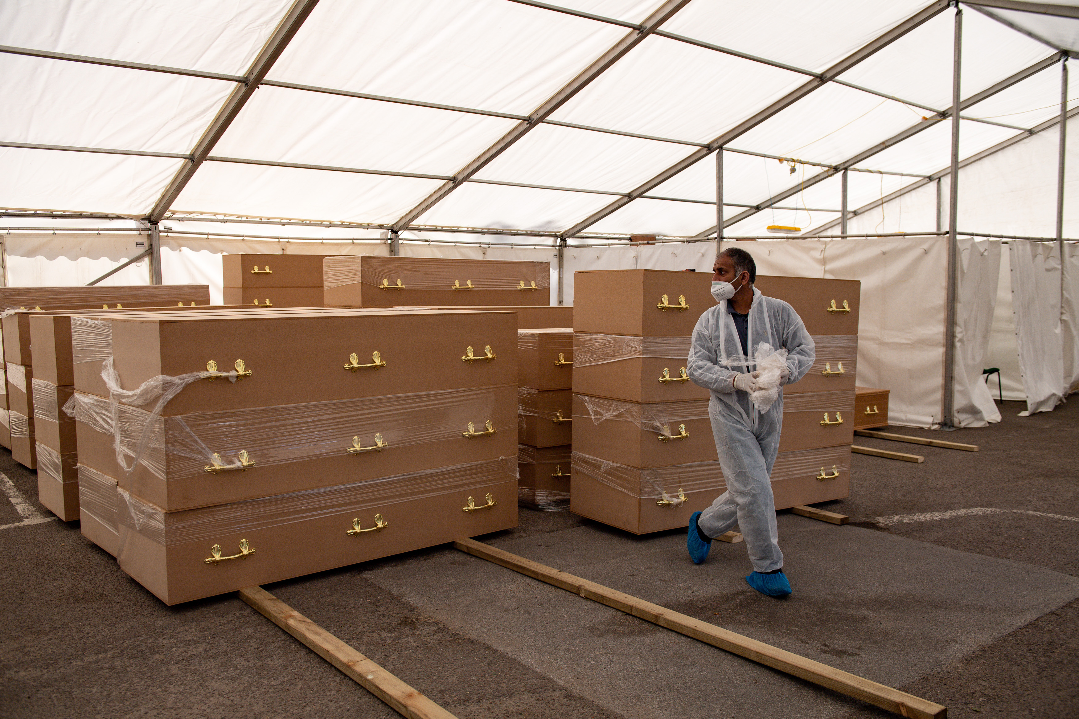 A volunteer walks by coffins at Central Jamia Mosque Ghamkol Sharif in Birmingham, which is operating a temporary morgue during the Covid-19 pandemic. 