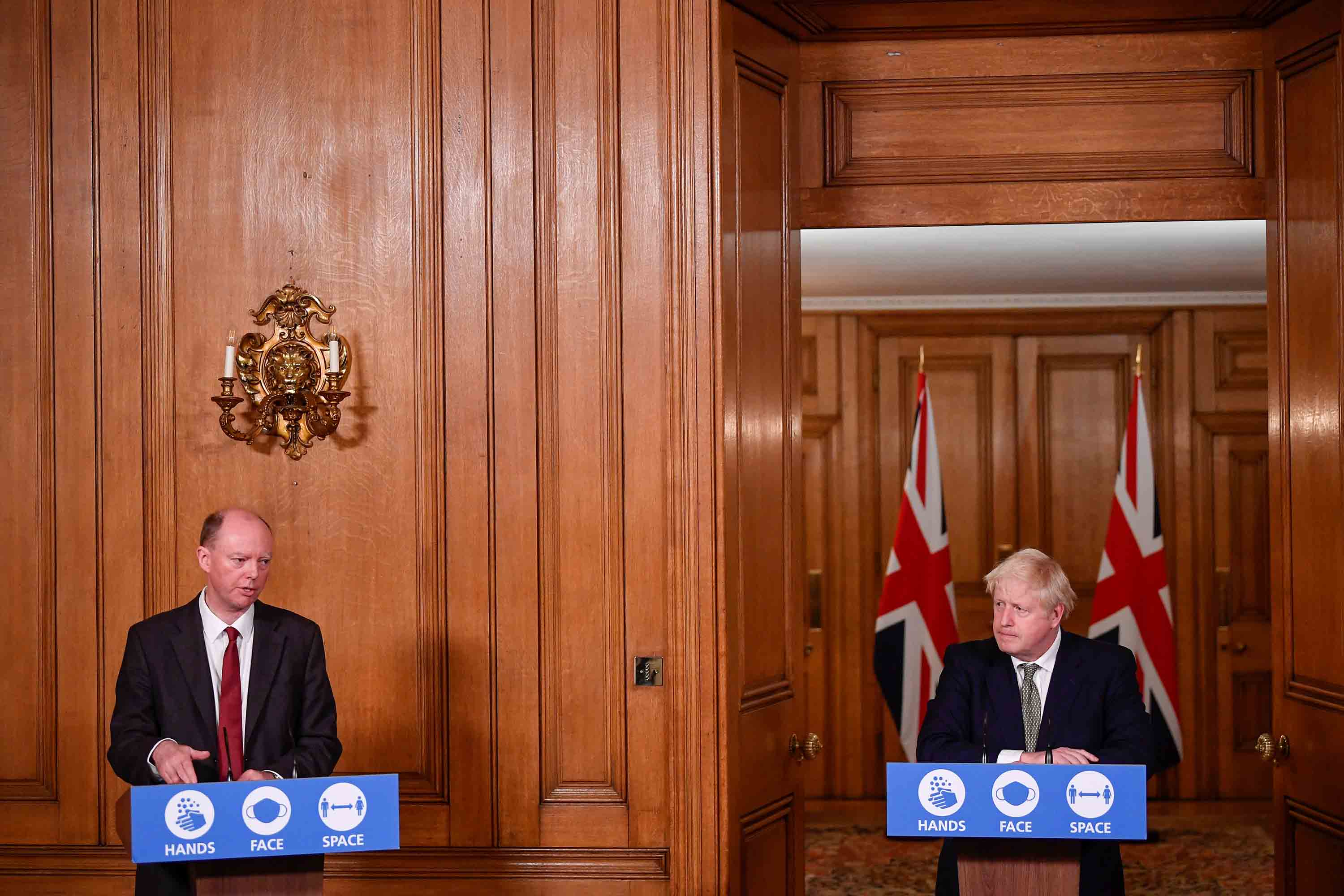 رئيس الوزراء بوريس جونسون ، إلى اليمين ، ينظر إلى منصب كبير المسؤولين الطبيين في إنجلترا ، يتحدث كريس ويتي خلال إحاطة افتراضية تحدد قواعد Covid-19 الجديدة ، في داونينج ستريت في لندن ، في 12 أكتوبر.