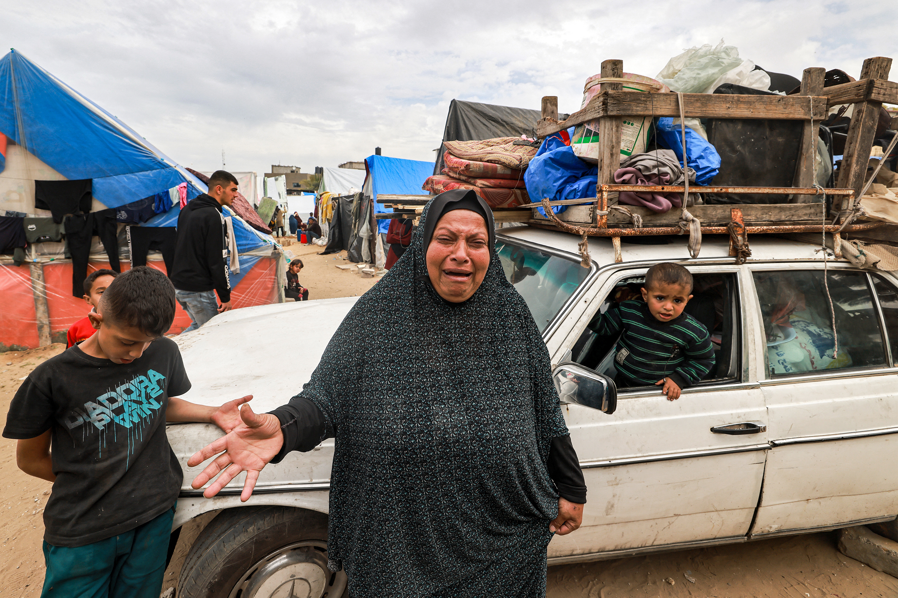 A woman reacts as she stands before a vehicle loaded with items secured by rope as people flee from Rafah, Gaza on February 13.