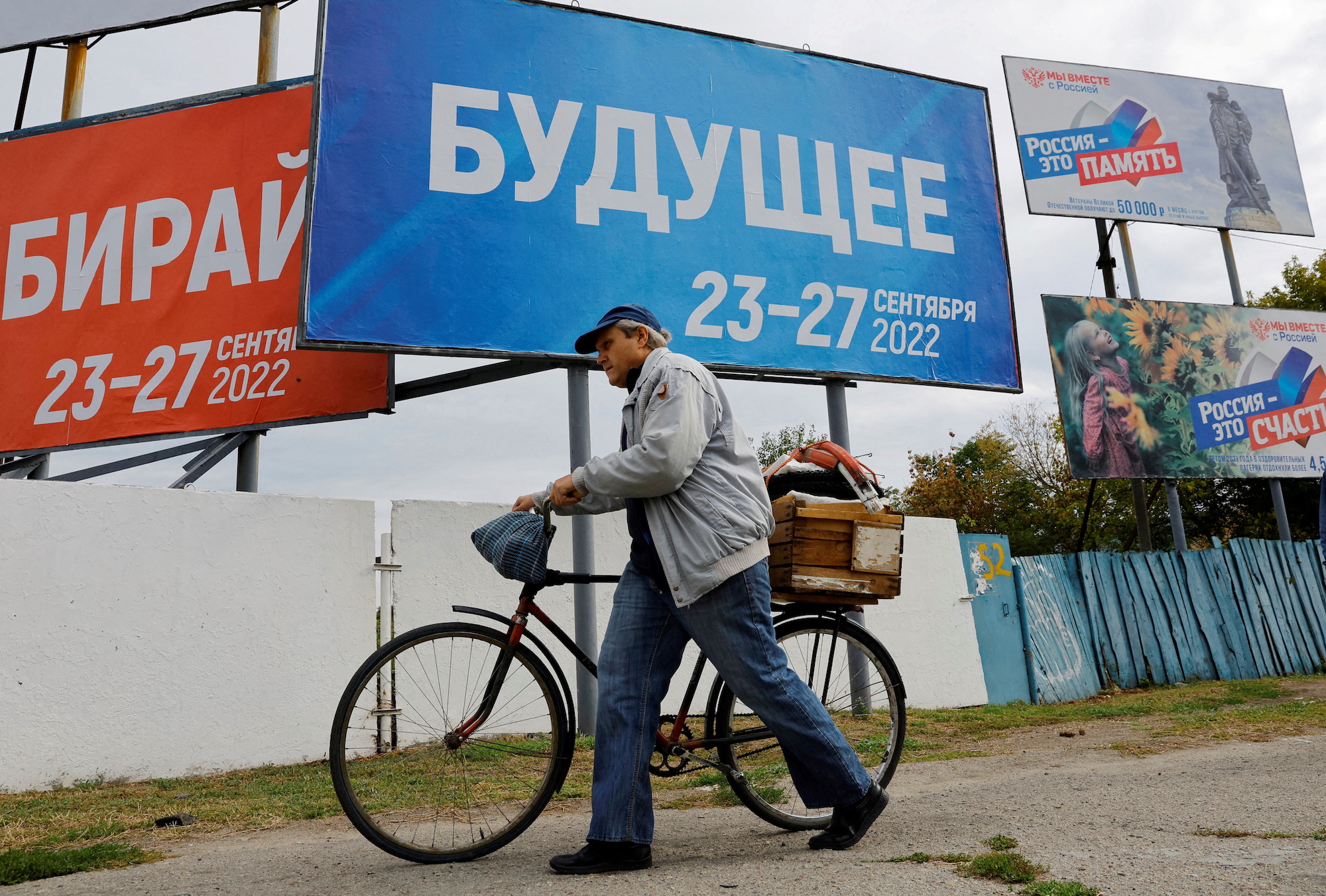 A man walks with his bicycle past election billboards in Russian-controlled Melitopol on September 26, 2022.