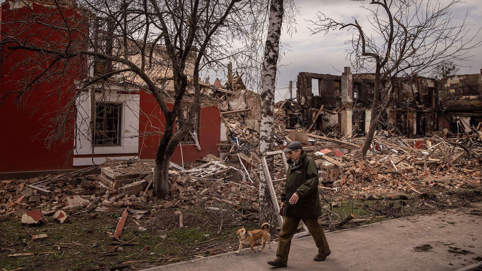 4 月 14 日，乌克兰哈尔科夫，一名男子牵着他的狗走过最近被俄罗斯炮击毁坏的建筑物。