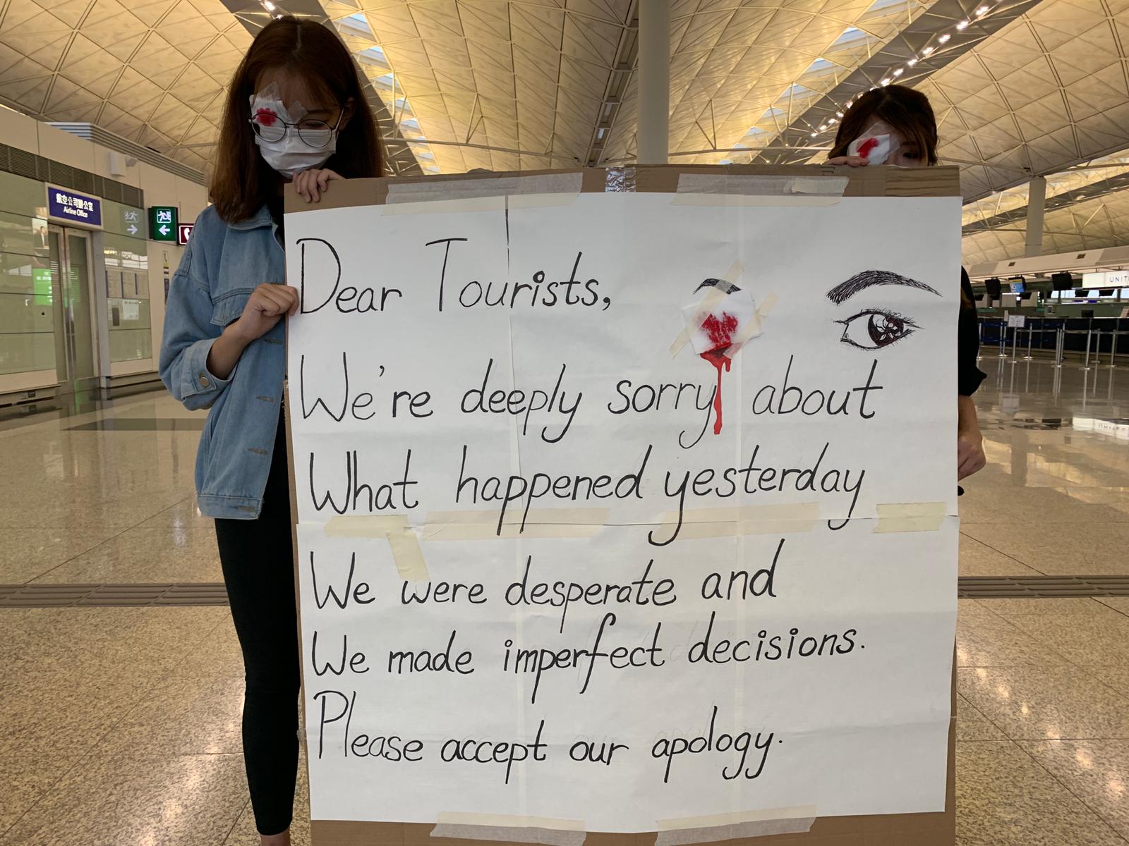 Two protesters hold an apology sign in the departures hall. 