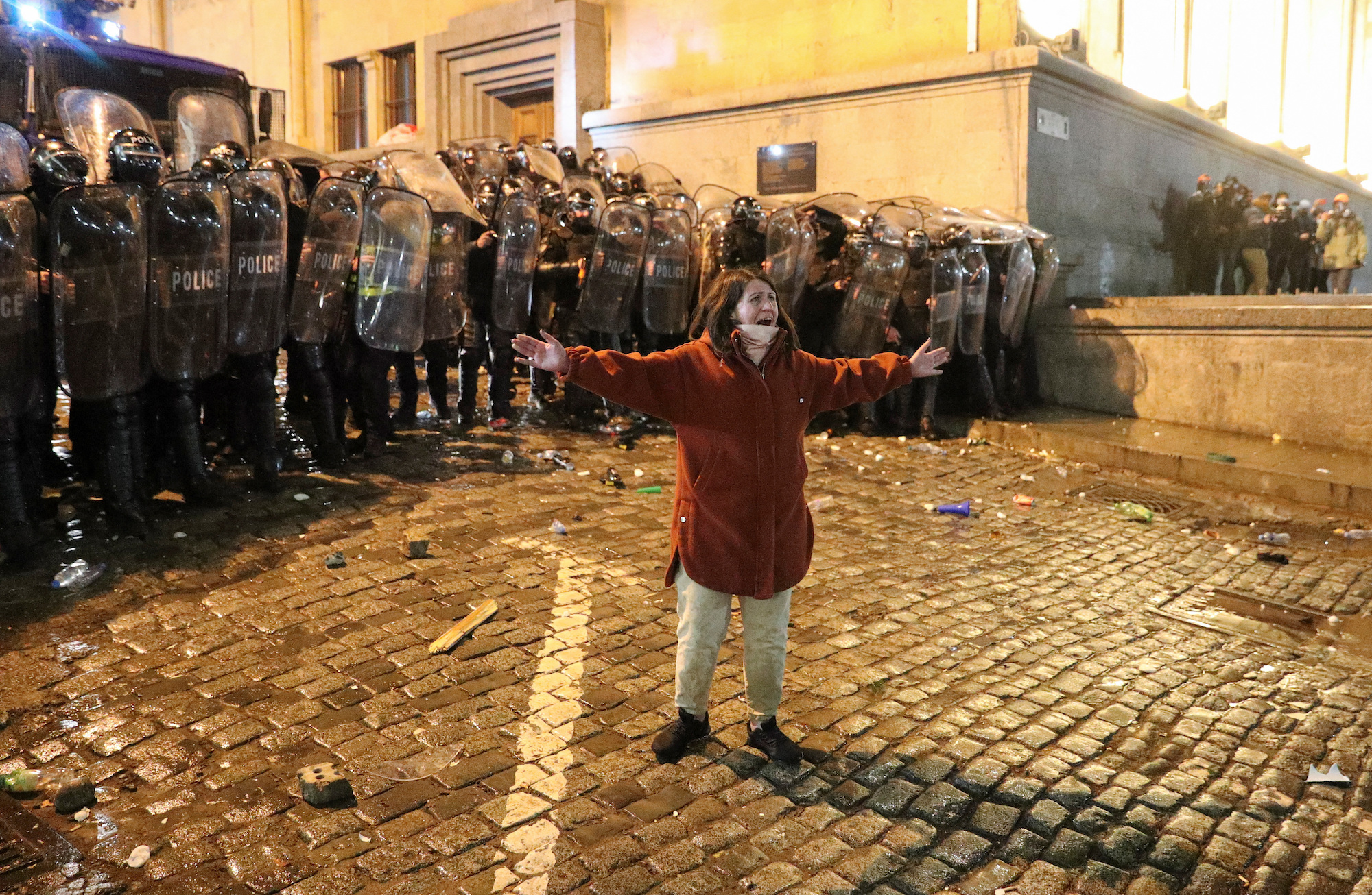 A woman reacts while standing in front of riot police who are blocking the street.