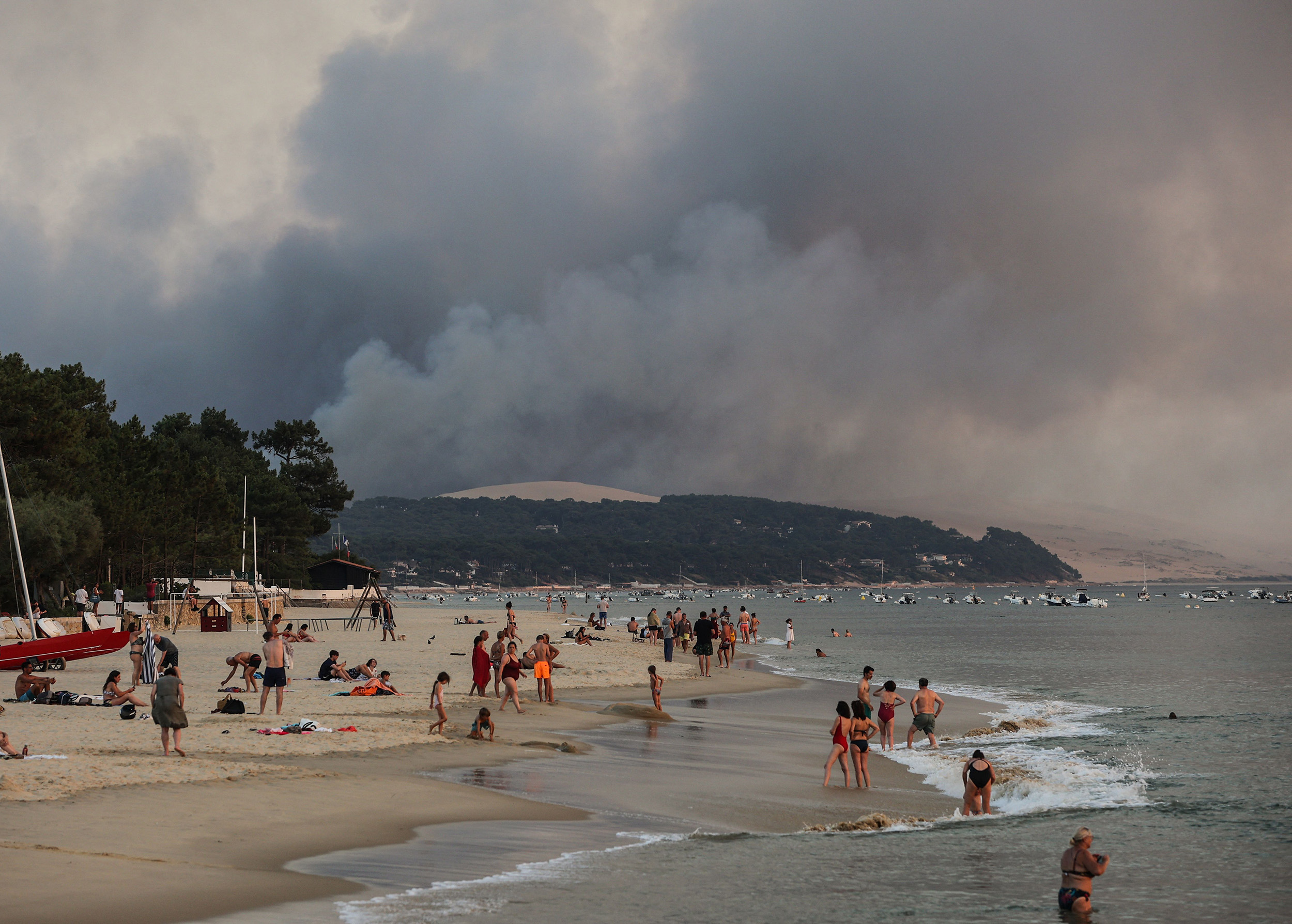 People gather at Moulleau beach as the smoke rises from the forest fire in La Teste-de-Buch, south west France, on July 18.