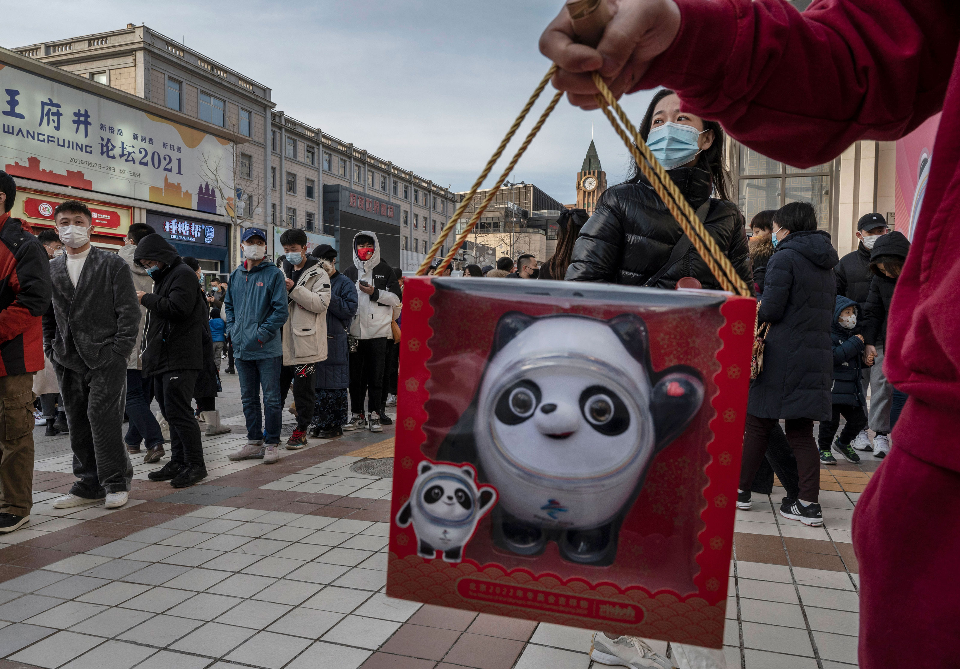 A man holds a replica of mascot Bing Dwen Dwen as people line up at the official 2022 Winter Olympics flagship store on Feb. 6, in Beijing.