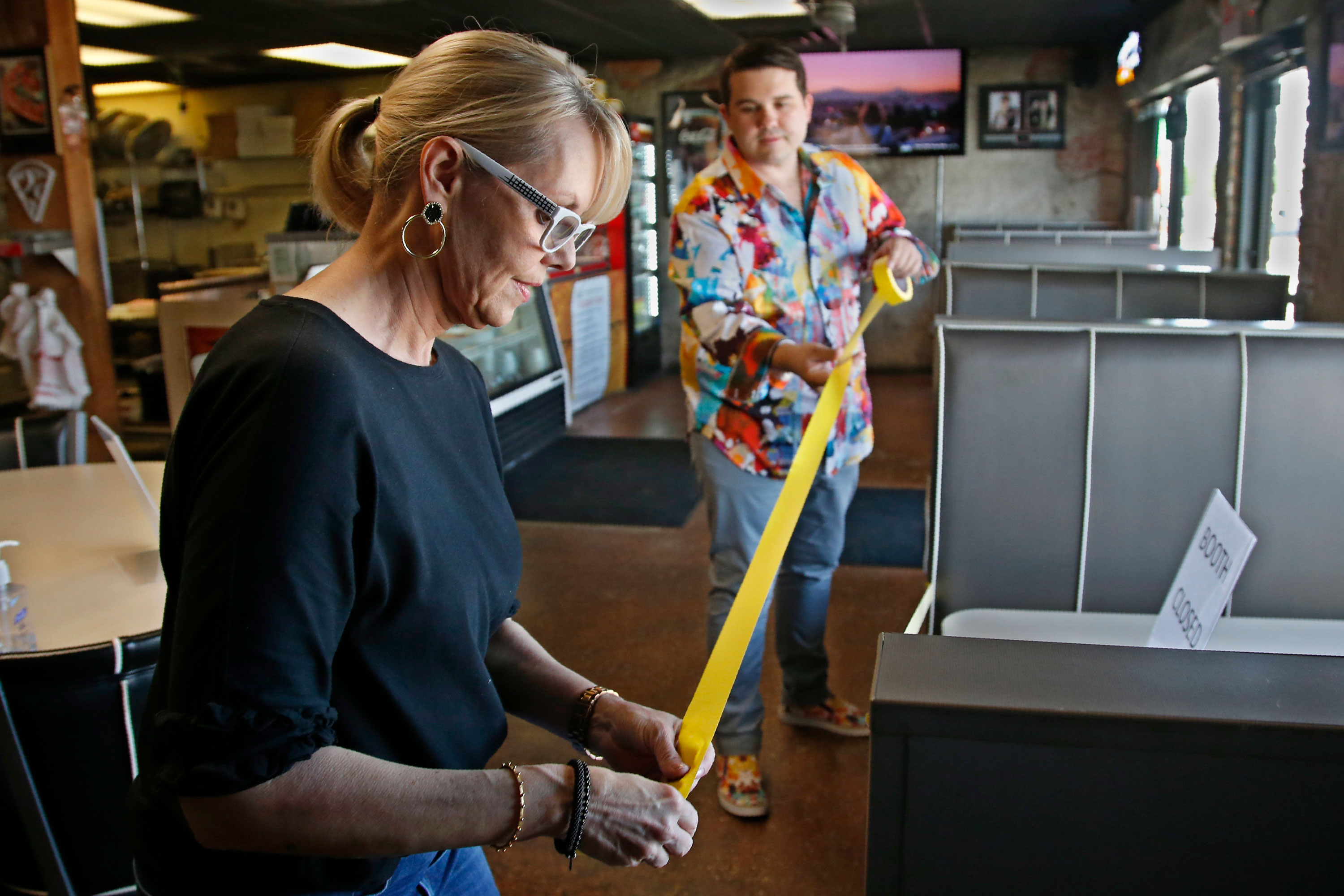 Leslie Wilson helps her son and owner of Falcone's Pizzeria, JP Wilson, tape off booths at his restaurant to provide social distancing, on April 30, in Oklahoma City, as they prepare to open the dining room to customers.