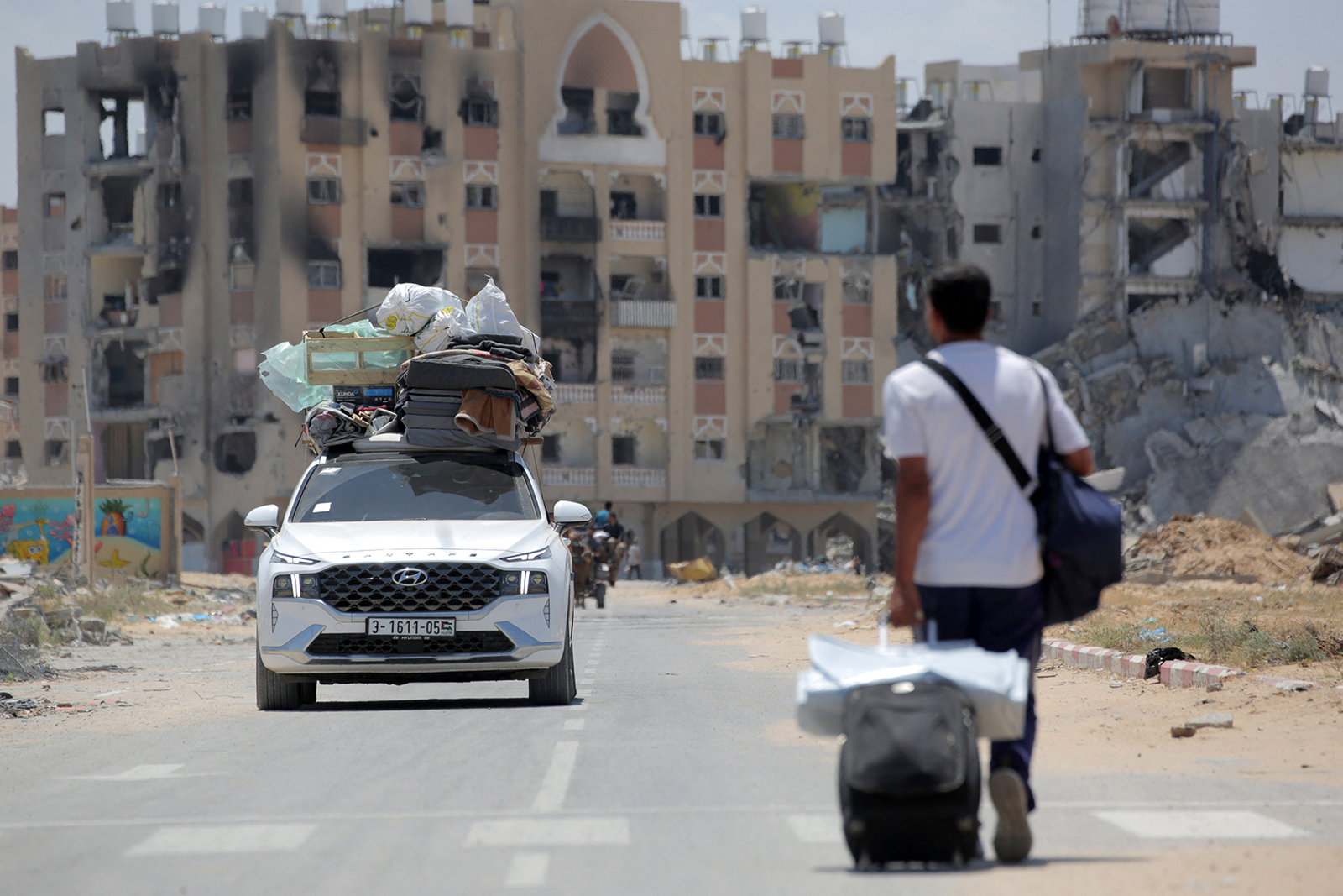 פלסטינים שנמלטו מרפיח בדרום רצועת עזה נושאים את חפציהם מאחורה של משאית כשאדם מושך את מזוודתו עם הגעתם לתפוס מחסה בחאן יונס ב-12 במאי.