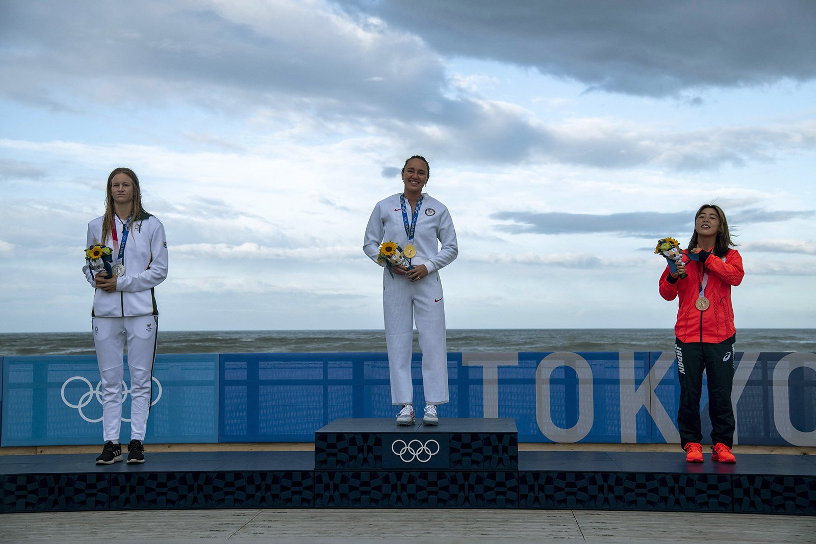 Gold medalist Carissa Moore, center, South Africa's Bianca Buitendag, left, Silver medalist, and Japan's Amuro Tsuzuki celebrate on the podium at the Tsurigasaki Surfing Beach, on July 27. 
