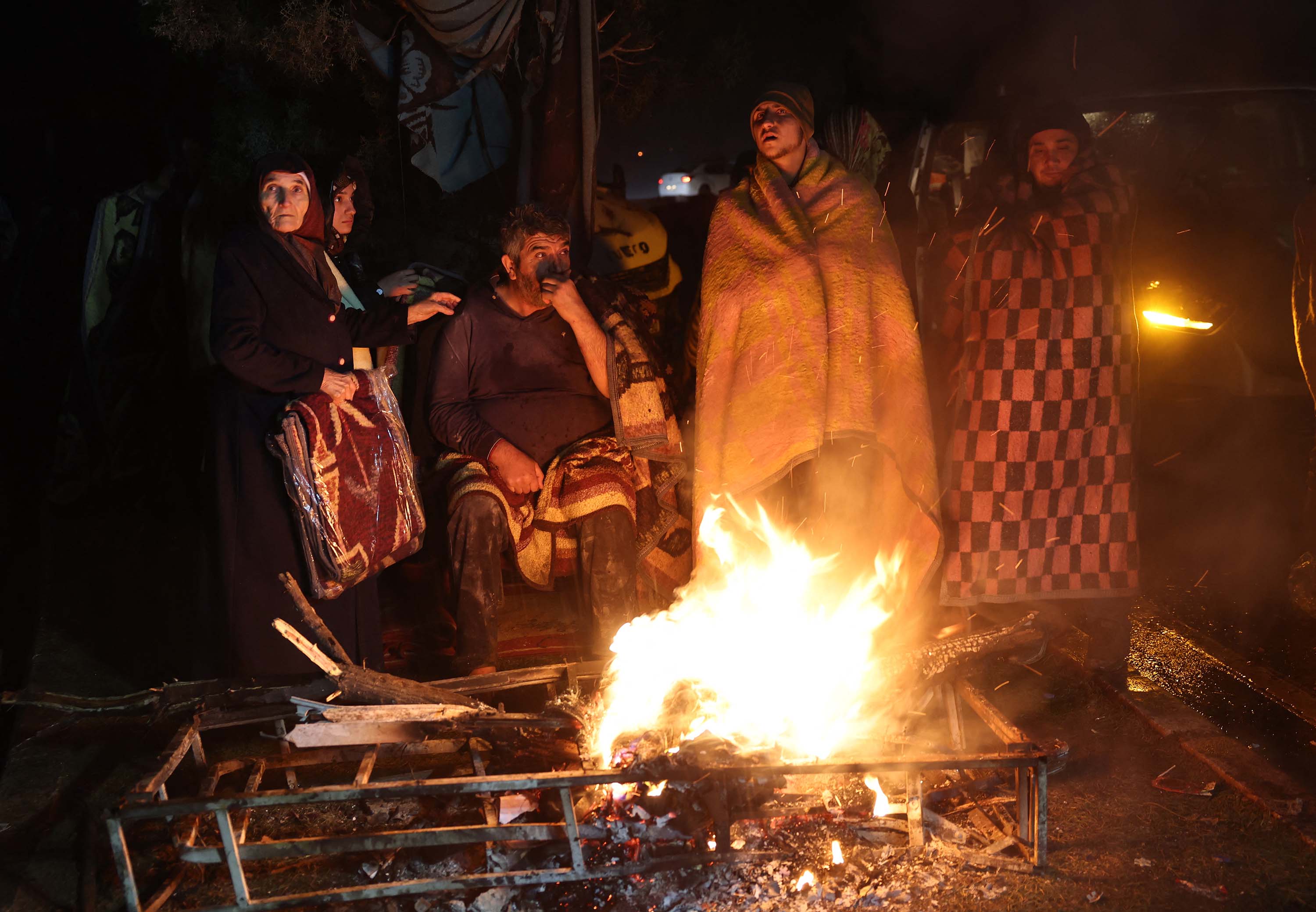 People warm themselves around a fire in Kahramanmaras, Turkey, on February 7, in the aftermath of the earthquake. 