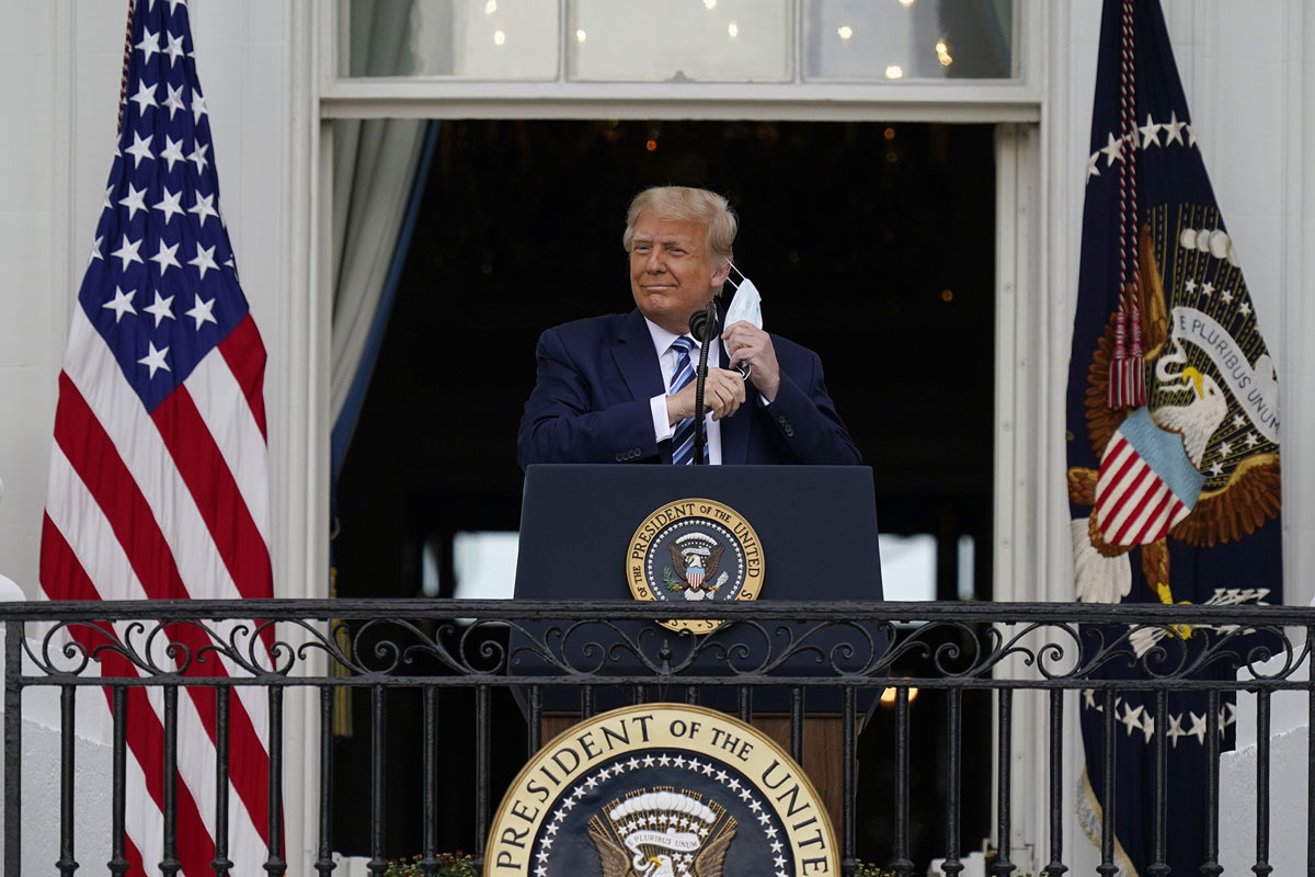President Donald Trump removes his face mask to speak from the Blue Room Balcony of the White House to a crowd of supporters, Saturday, October 10.