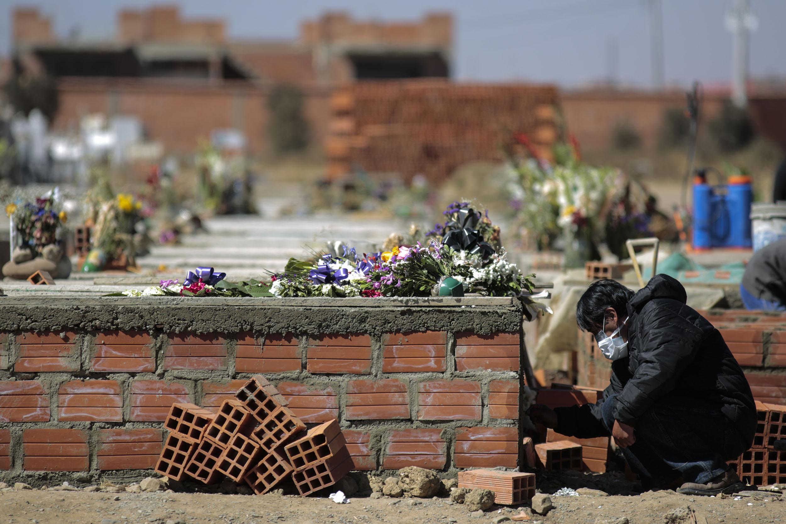 A mourner writes the name of the deceased on the fresh cement at Mercedario Cemetery on July 29, in El Alto, Bolivia. 